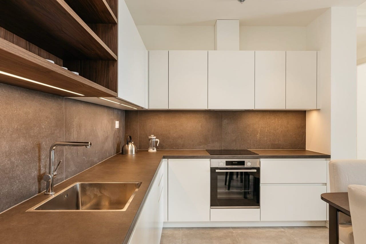 Modern kitchen with white cabinets and a dark countertop in Lustica Bay apartments, Radovici, Montenegro.