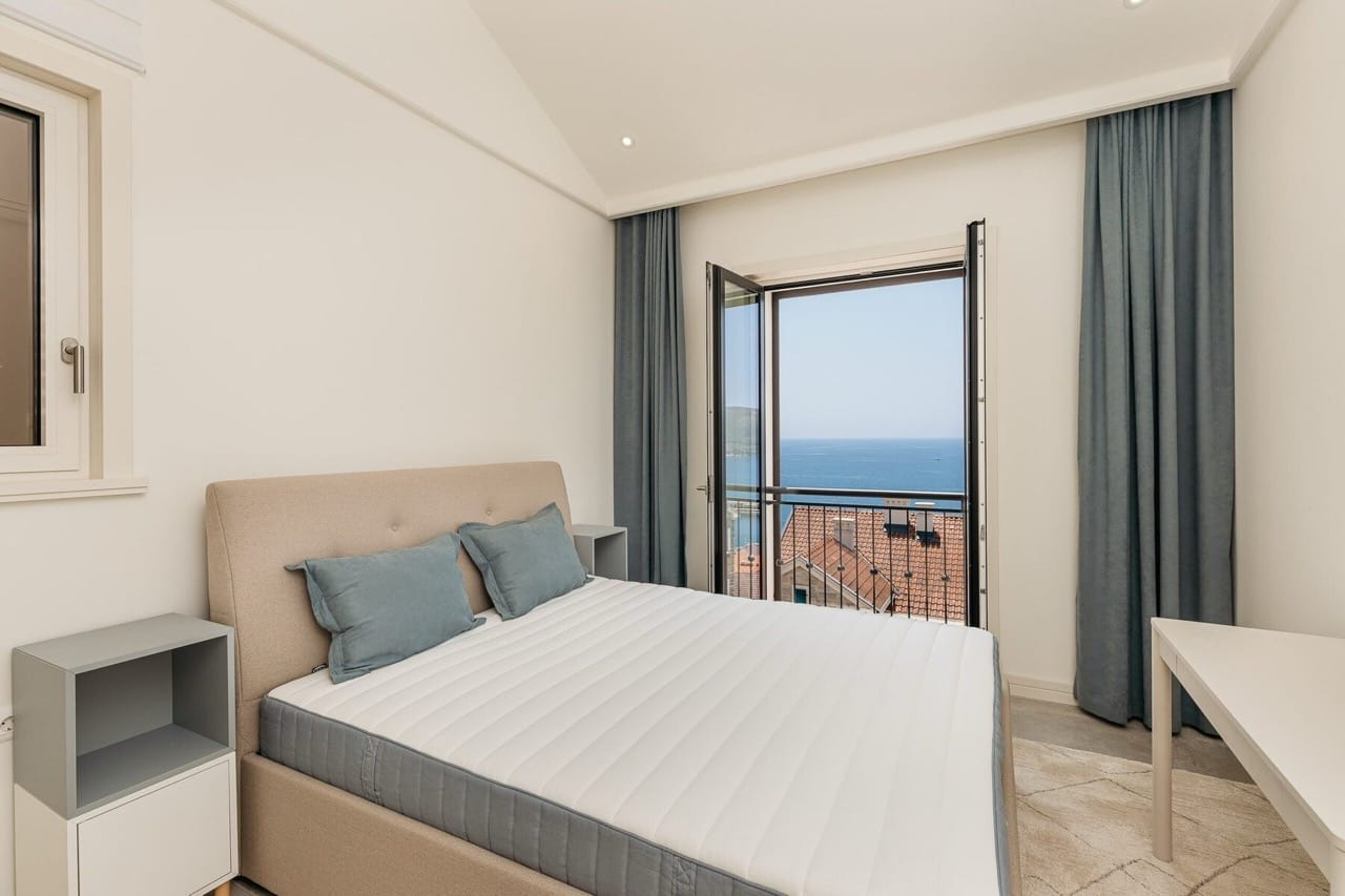 Bedroom in an apartment in Luštica Bay, Radovići, Montenegro: double bed, panoramic sea view and terracotta roofs.