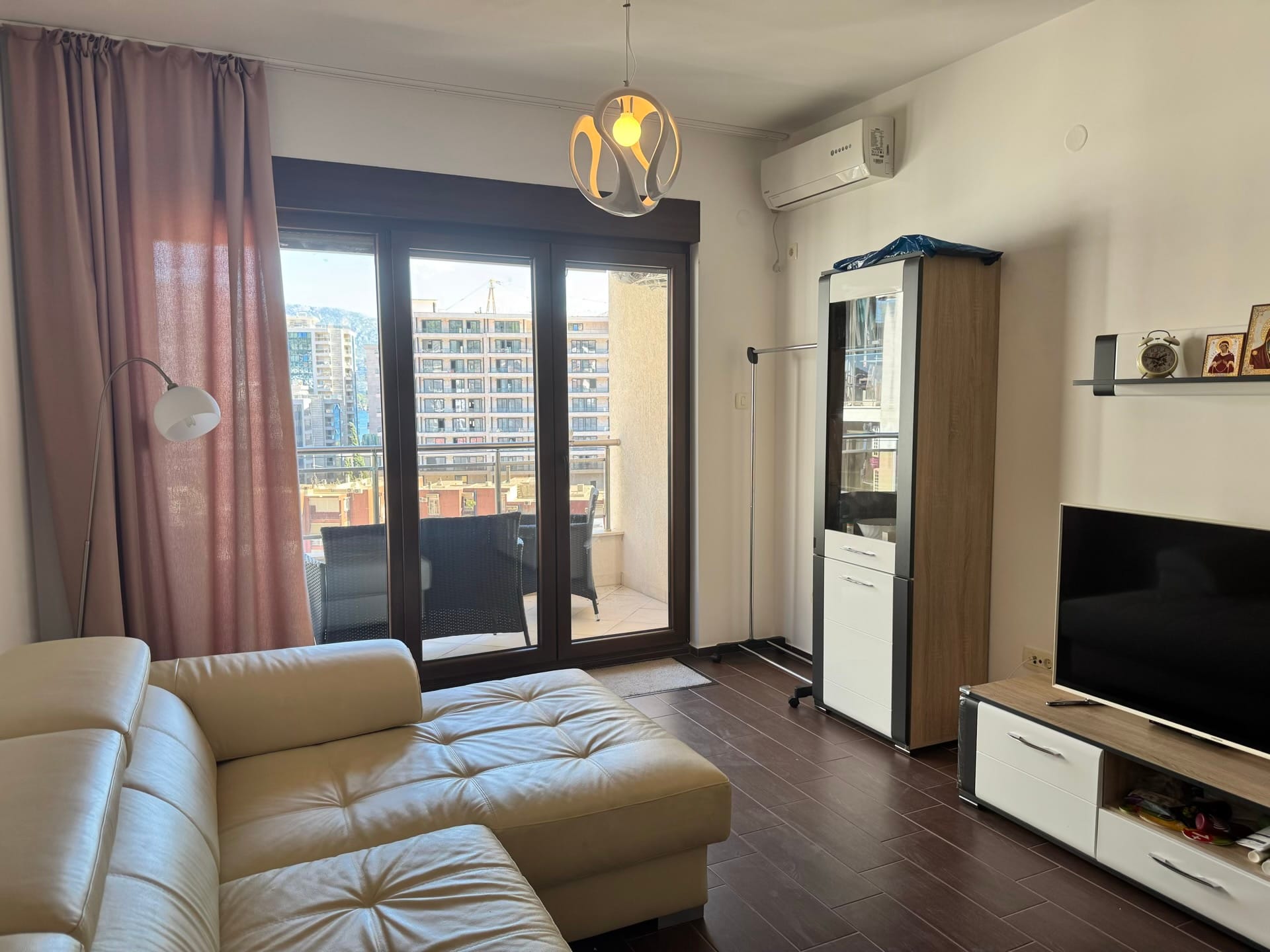 Dnevna soba u stanu u Budvi, Crna Gora: svetla sofa, moderan nameštaj, izlaz na terasu s pogledom na grad.
