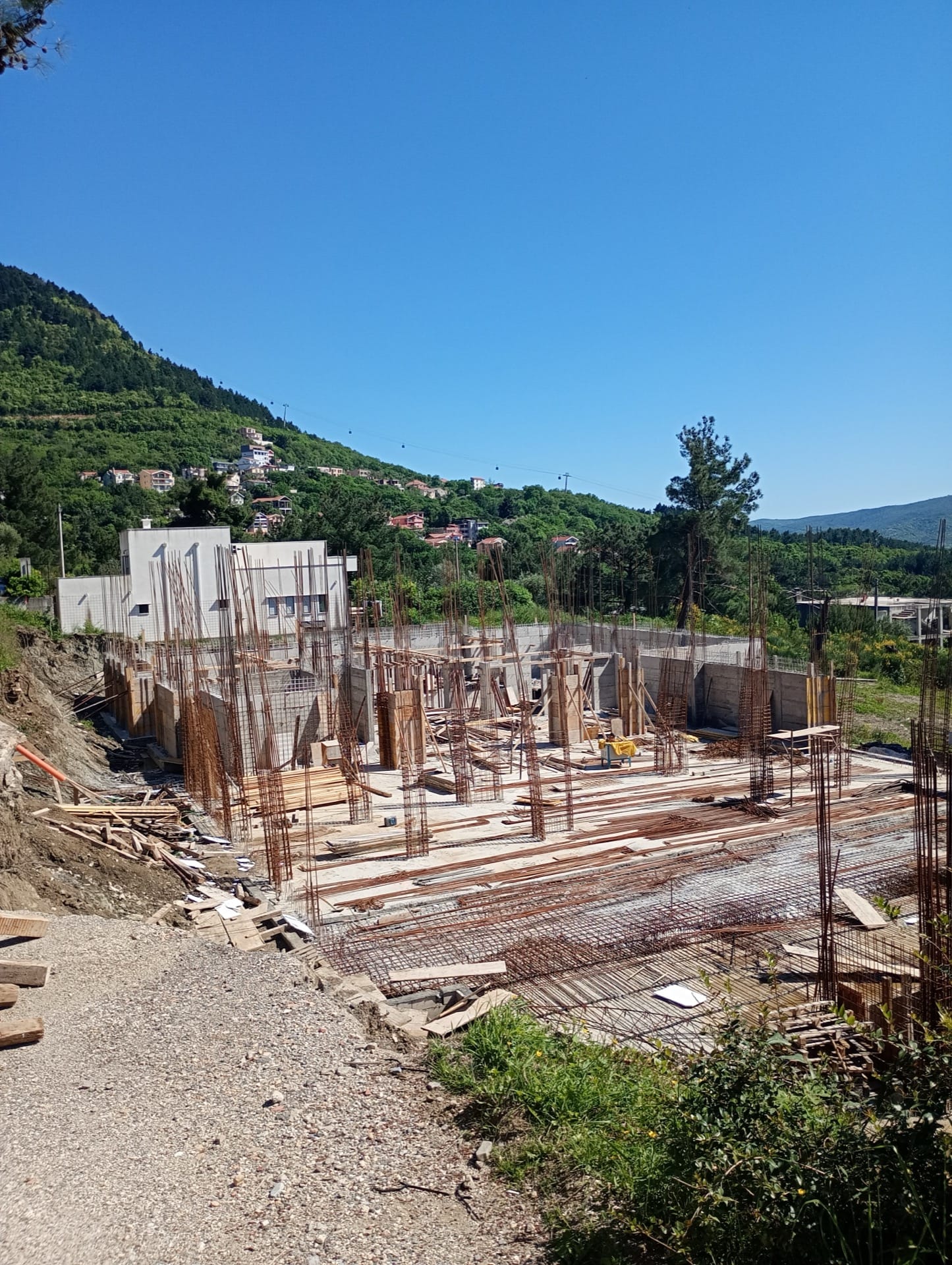 Izgradnja stambenog kompleksa u Budvi, Crna Gora: armiranobetonski okvir temelja i pogled na planine.