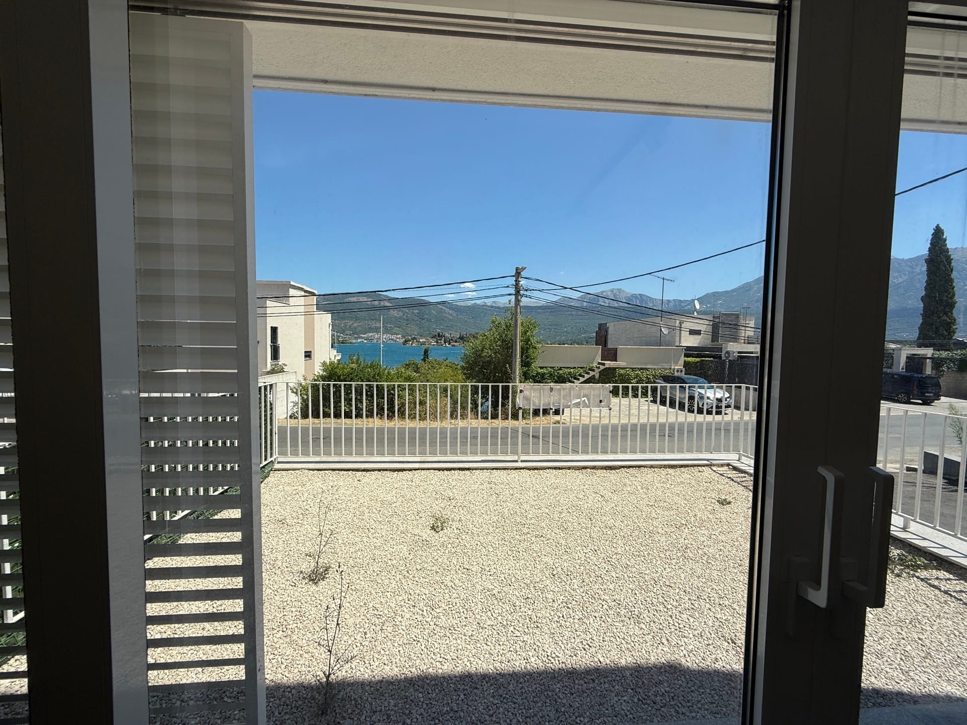 Pogled sa terase kuće u Đuraševićima, Crna Gora: šljunkovito dvorište, bela ograda i panorama mora sa planinama.