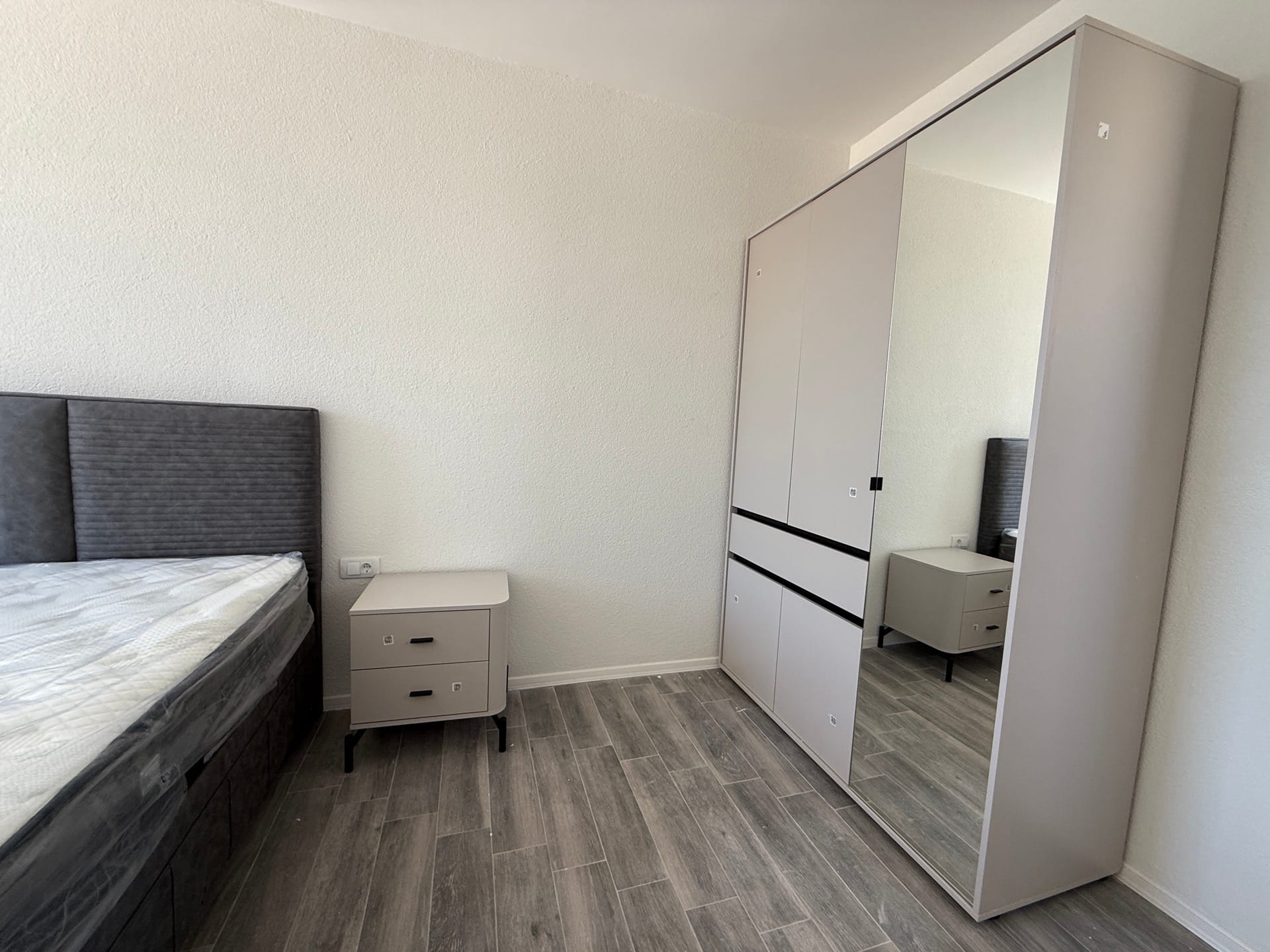 Spavaća soba u townhouseu, Luštica, Crna Gora: krevet sa sivim uzglavljem, noćni stočić i ormar sa ogledalom.
