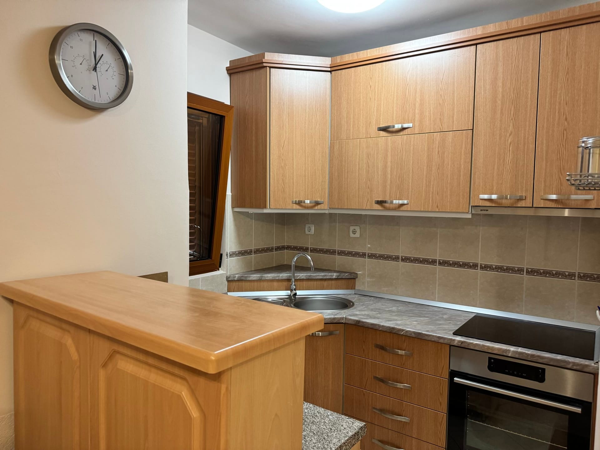 Ugaona kuhinja sa drvenim frontovima i barskim pultom u stanu, Budva, Crna Gora. Ugradni aparati i pločice.
