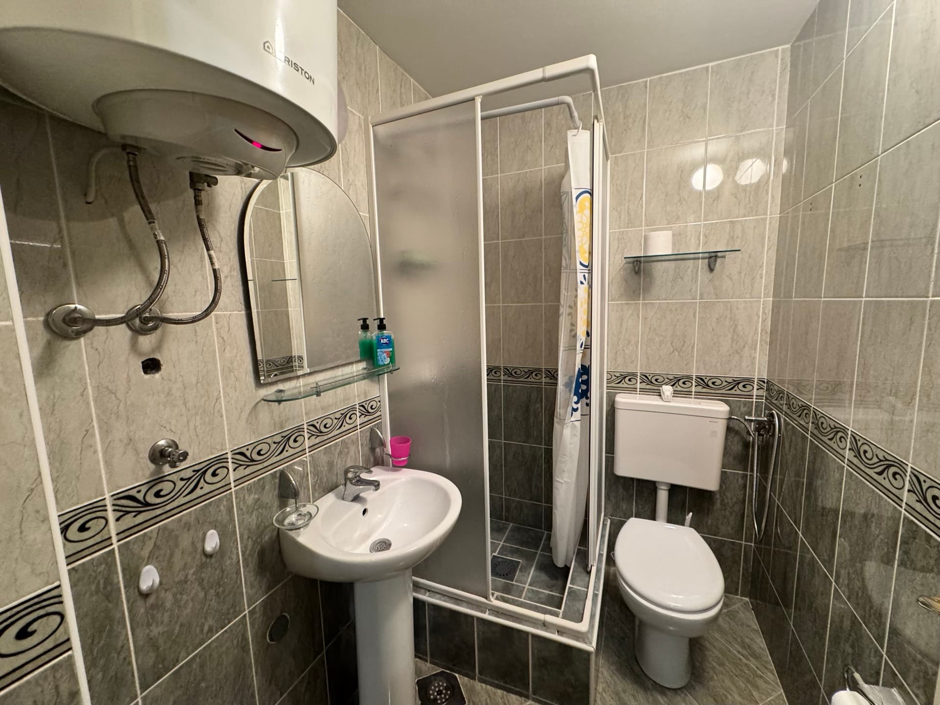 Kupatilo u stanu u Budvi, Crna Gora: tuš kabina, lavabo, WC šolja i Ariston bojler na zidu.
