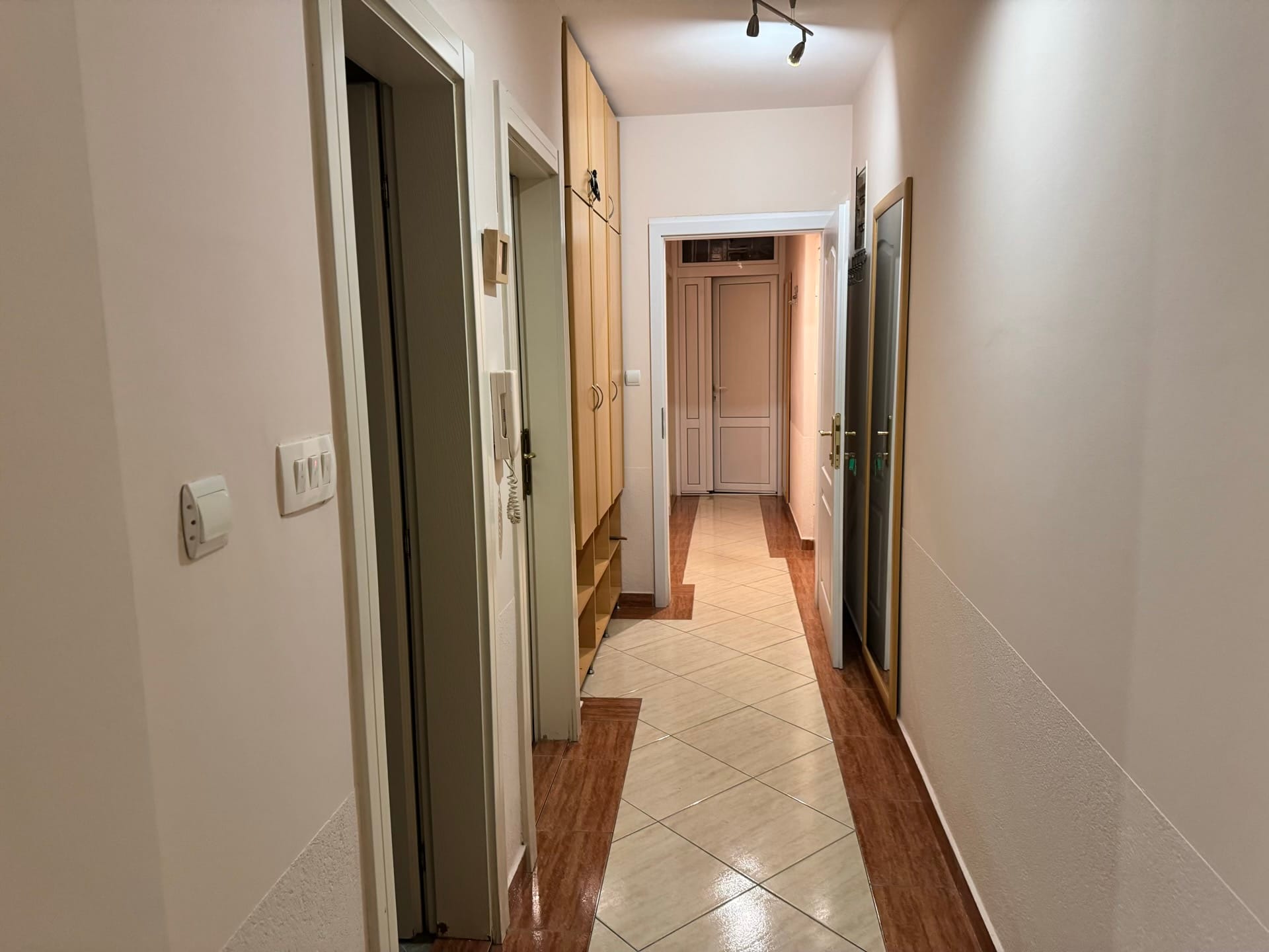 Svetao hodnik u stanu u Budvi, Crna Gora: ugradni ormar, pločice na podu i unutrašnja vrata.