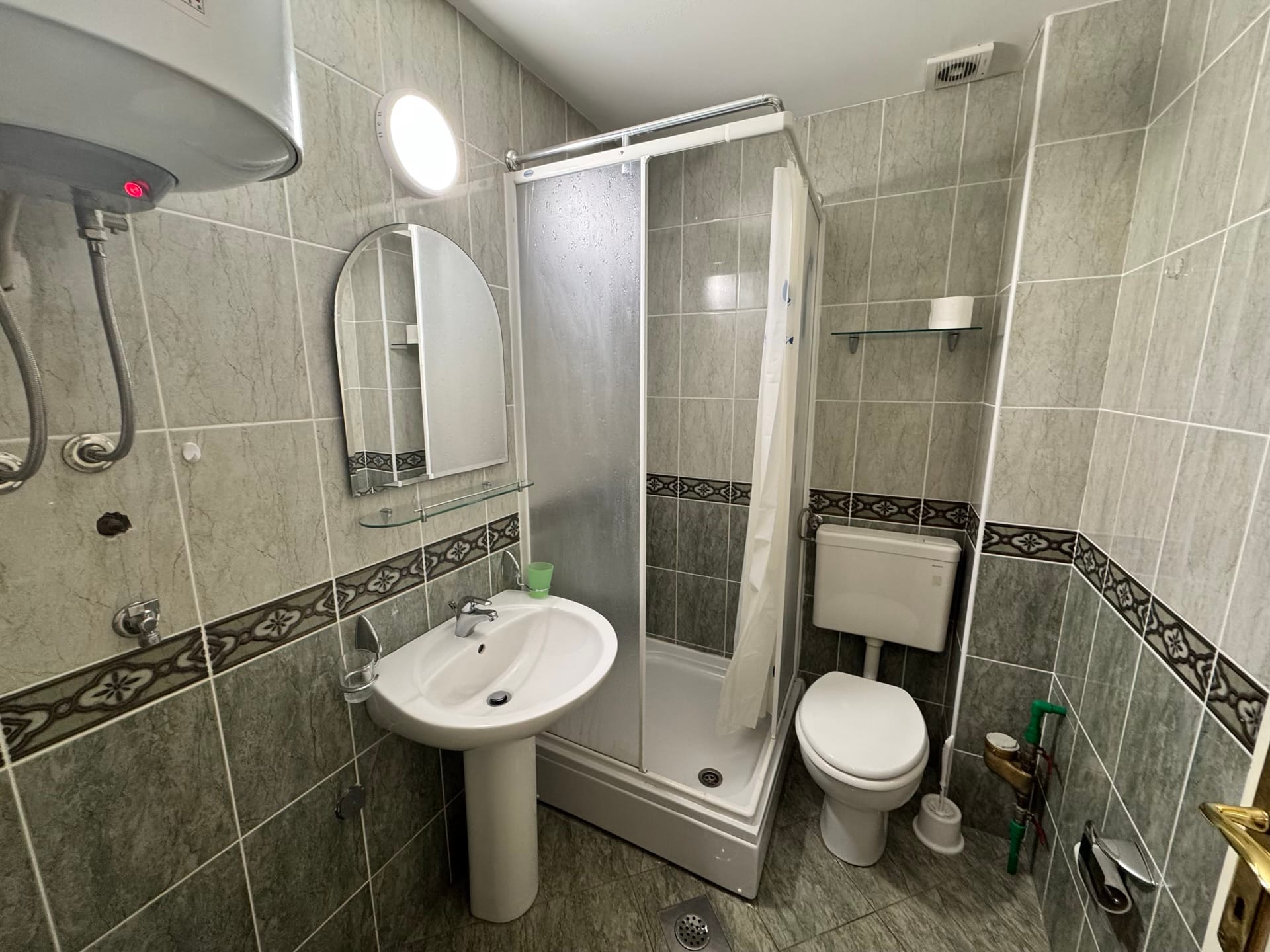 Kupatilo u stanu u Budvi, Crna Gora: tuš kabina, lavabo, WC šolja i obloga od sivih pločica.