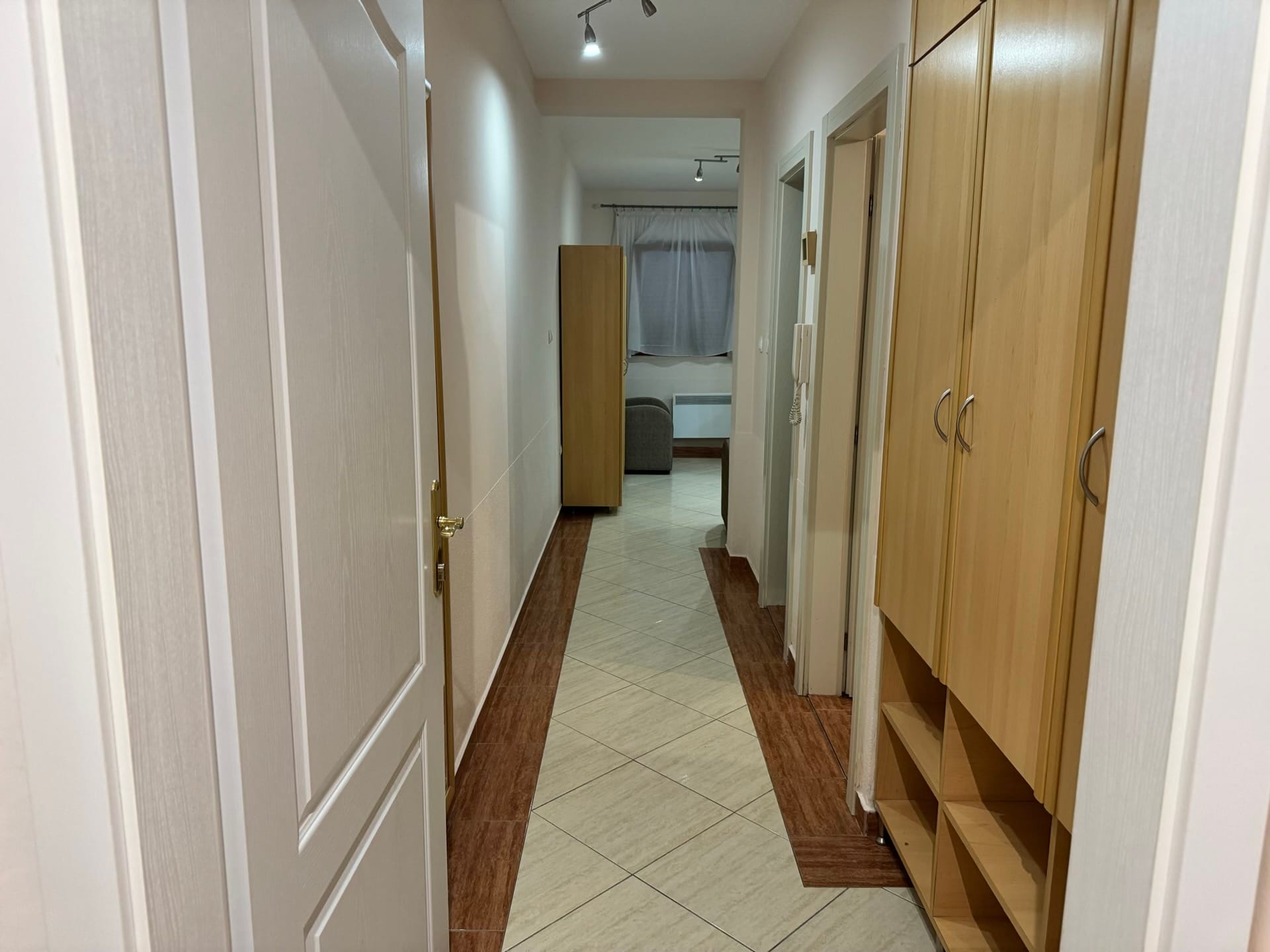 Svetao hodnik u stanu u Budvi, Crna Gora: ugradni ormar, pločice na podu i unutrašnja vrata.