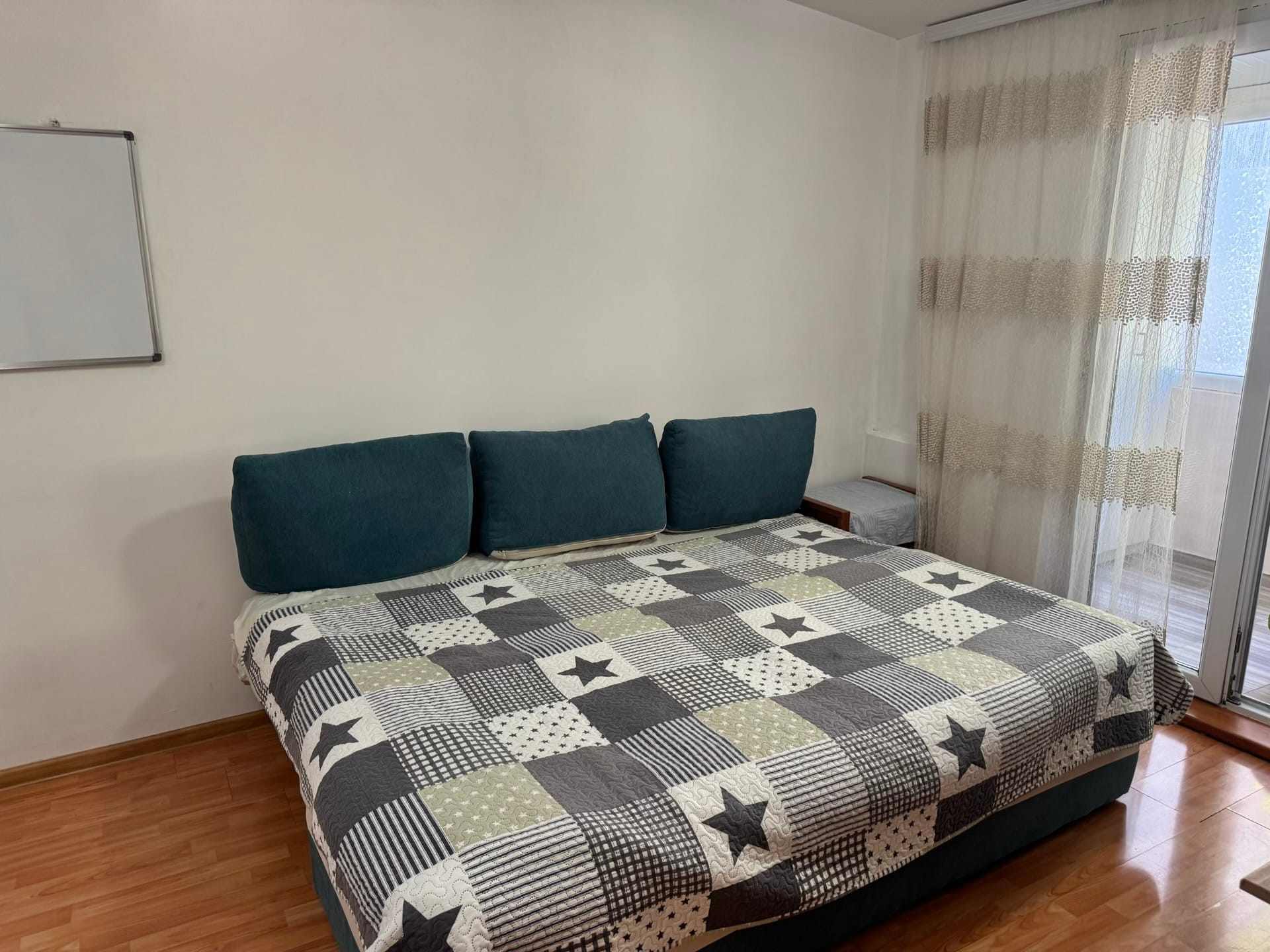 Spavaća soba sa bračnim krevetom u stanu u Bečićima, Crna Gora: parket, svetli zidovi, izlaz na balkon i tekstil.