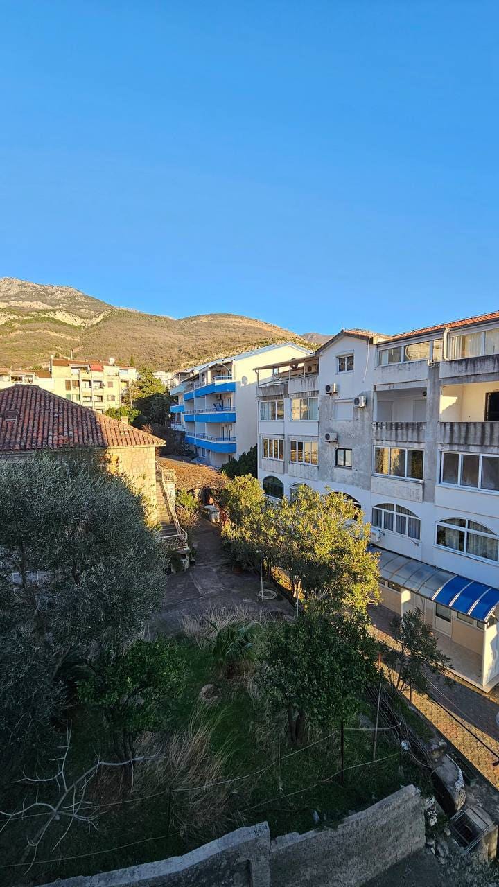 Pogled na stambeni kompleks i planine iz stana u Bečićima, Crna Gora: uređeno dvorište sa drvećem i zgradama.