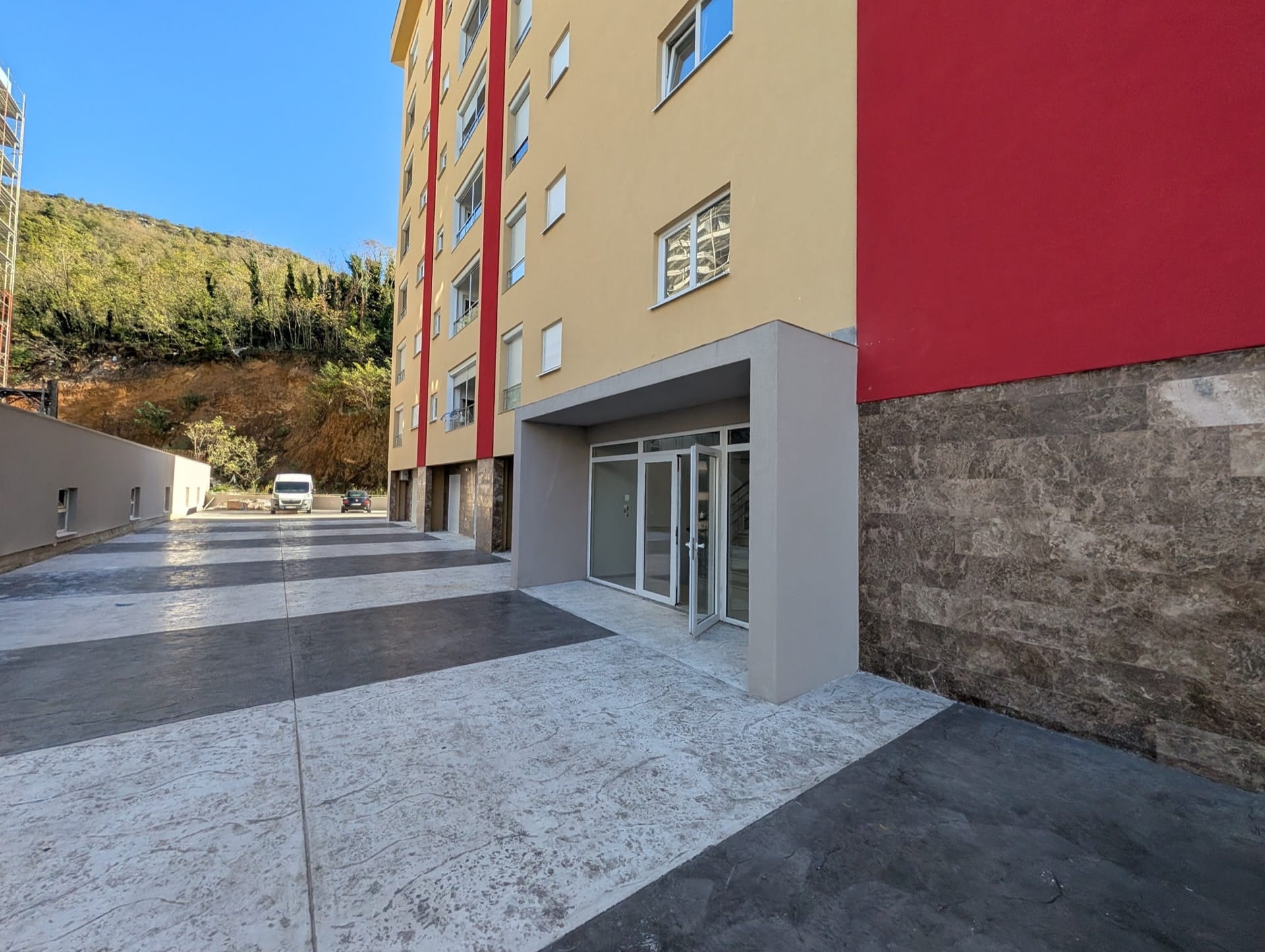 Ulaz u savremeni stambeni kompleks u Bečićima, Crna Gora: fasada obložena kamenom i parking pored zgrade.