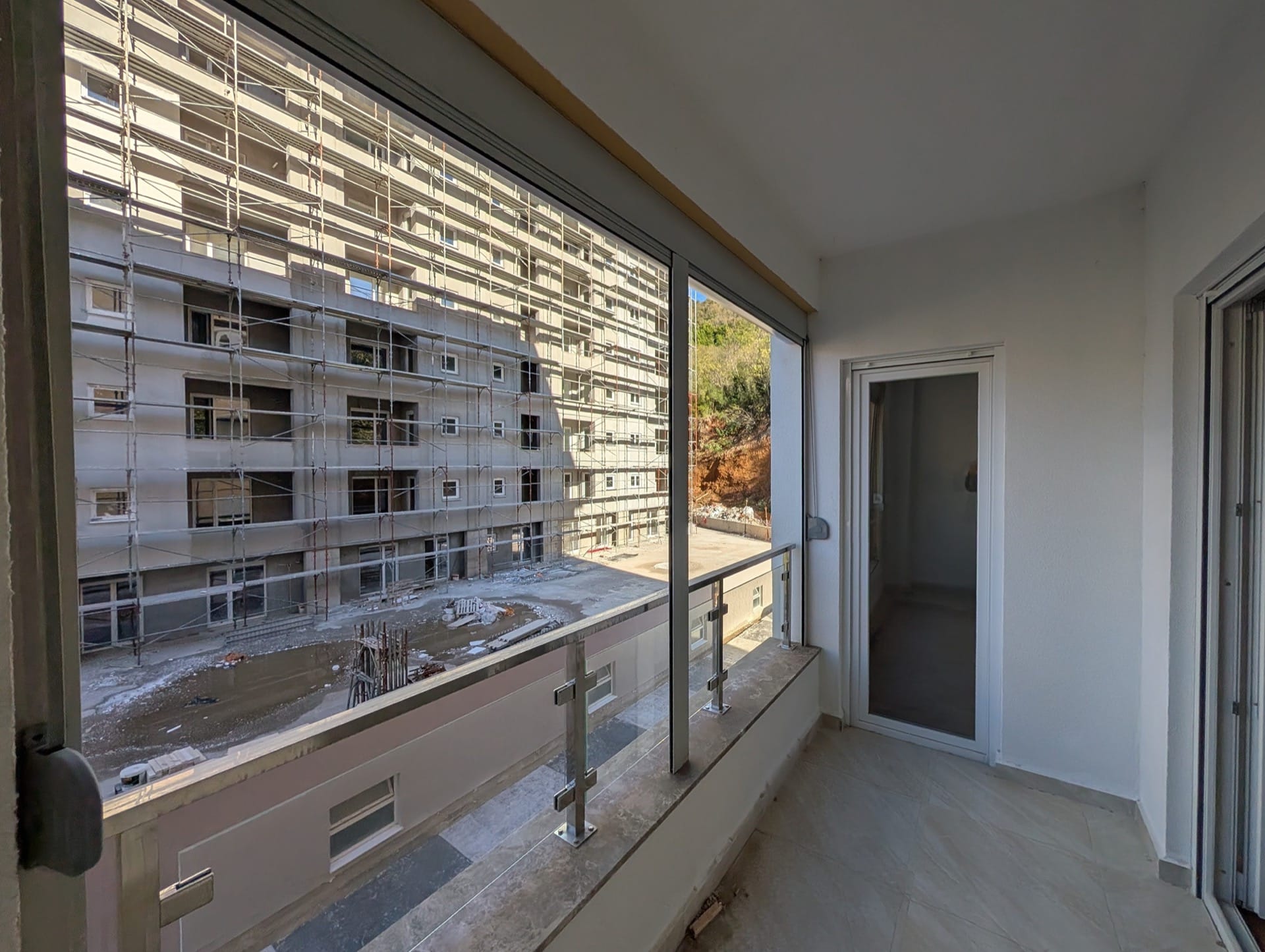 Balkon u stambenom kompleksu u izgradnji u Bečićima, Crna Gora: pogled na susednu zgradu u skelama i završna obrada pločicama.