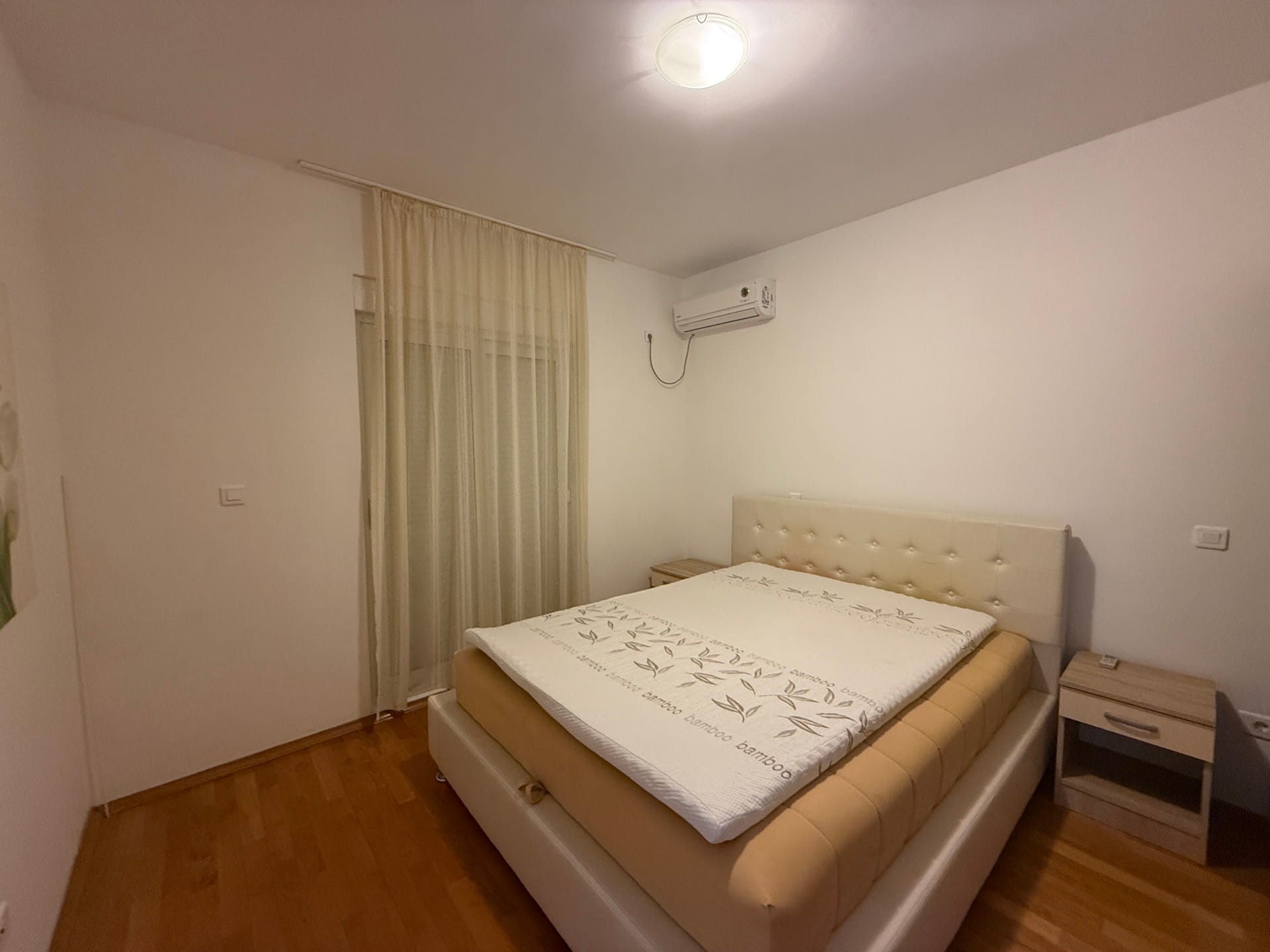 Svetla spavaća soba sa bračnim krevetom i klima-uređajem u stanu u Budvi, Crna Gora, sa izlazom na balkon.