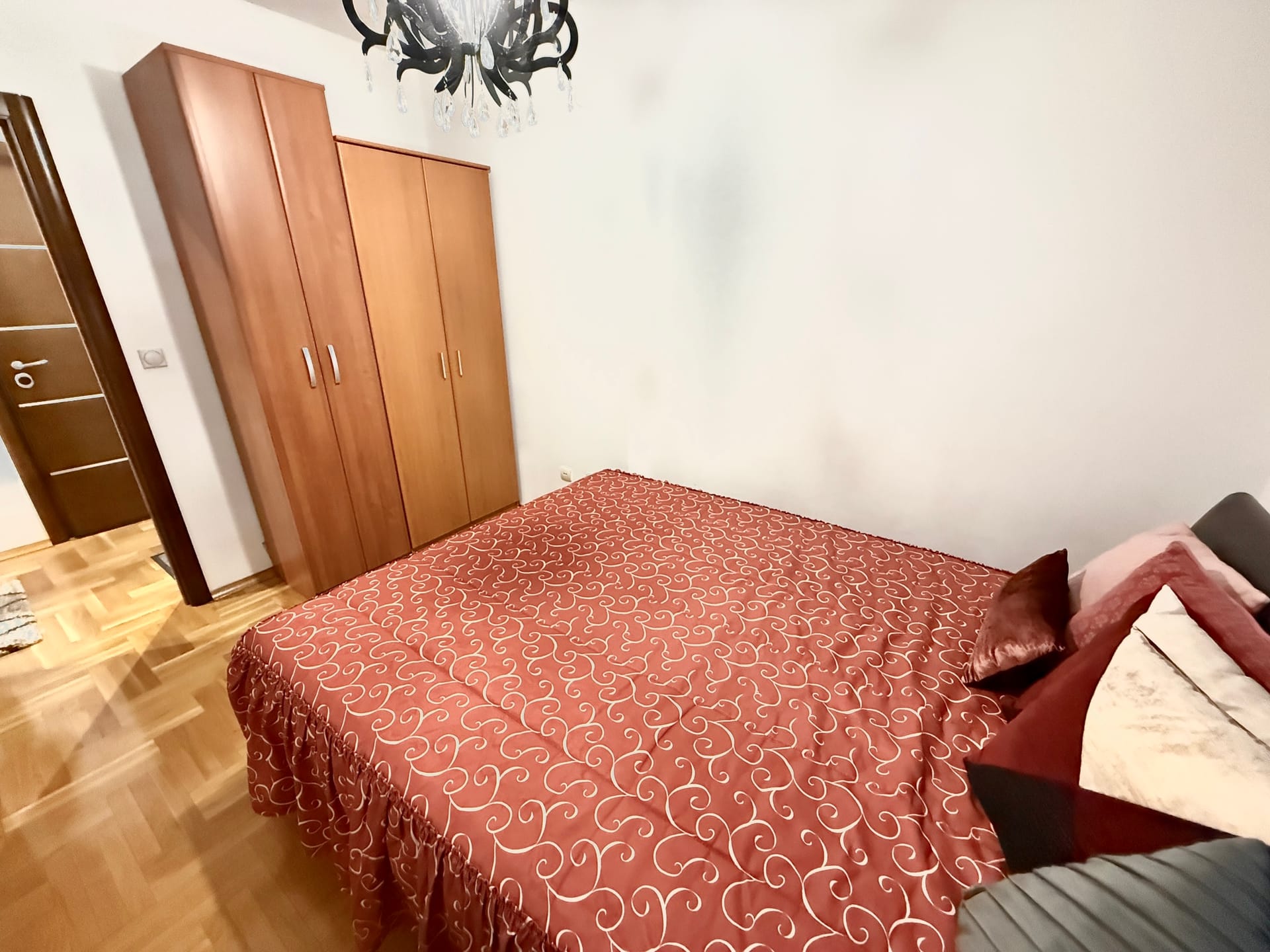 Spavaća soba u stanu u Budvi, Crna Gora: bračni krevet sa crvenim prekrivačem, drveni ormar i parket.