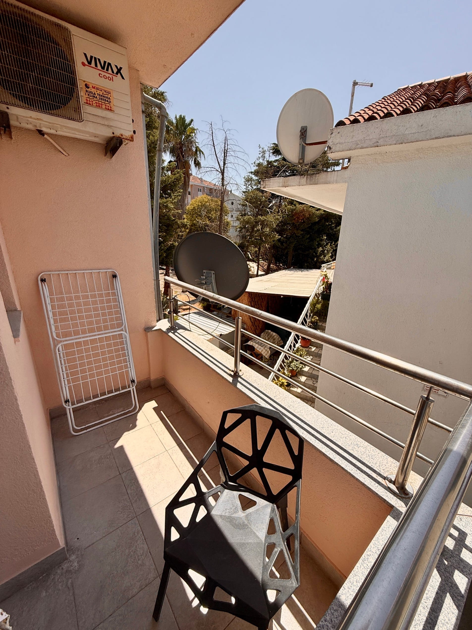 Balkon stana u Budvi, Crna Gora: moderna stolica, sušilica za veš, klima-uređaj i pogled na zeleno dvorište.
