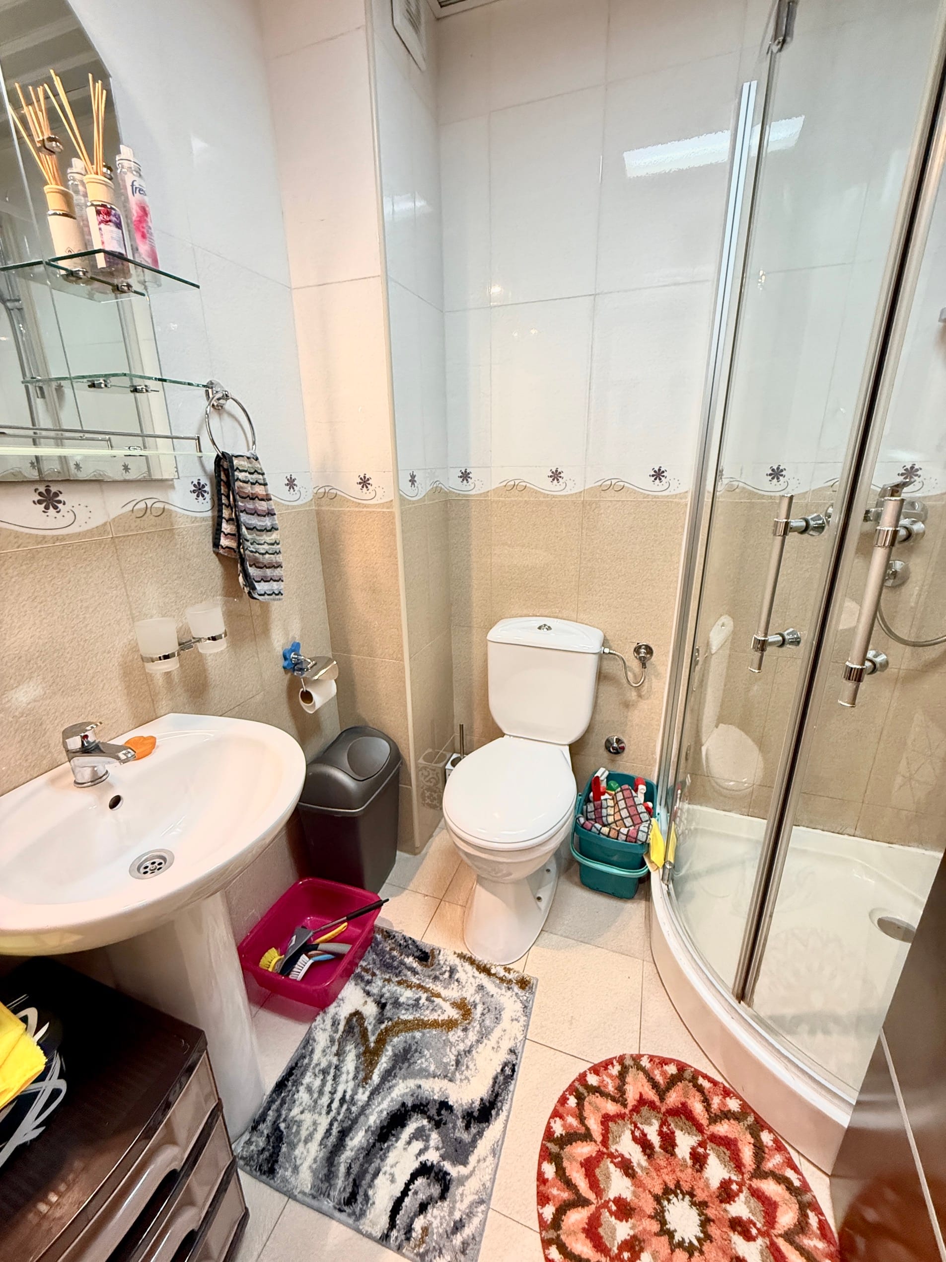Kupatilo u stanu u Budvi, Crna Gora: tuš kabina, lavabo, WC šolja i svetla obloga od pločica.