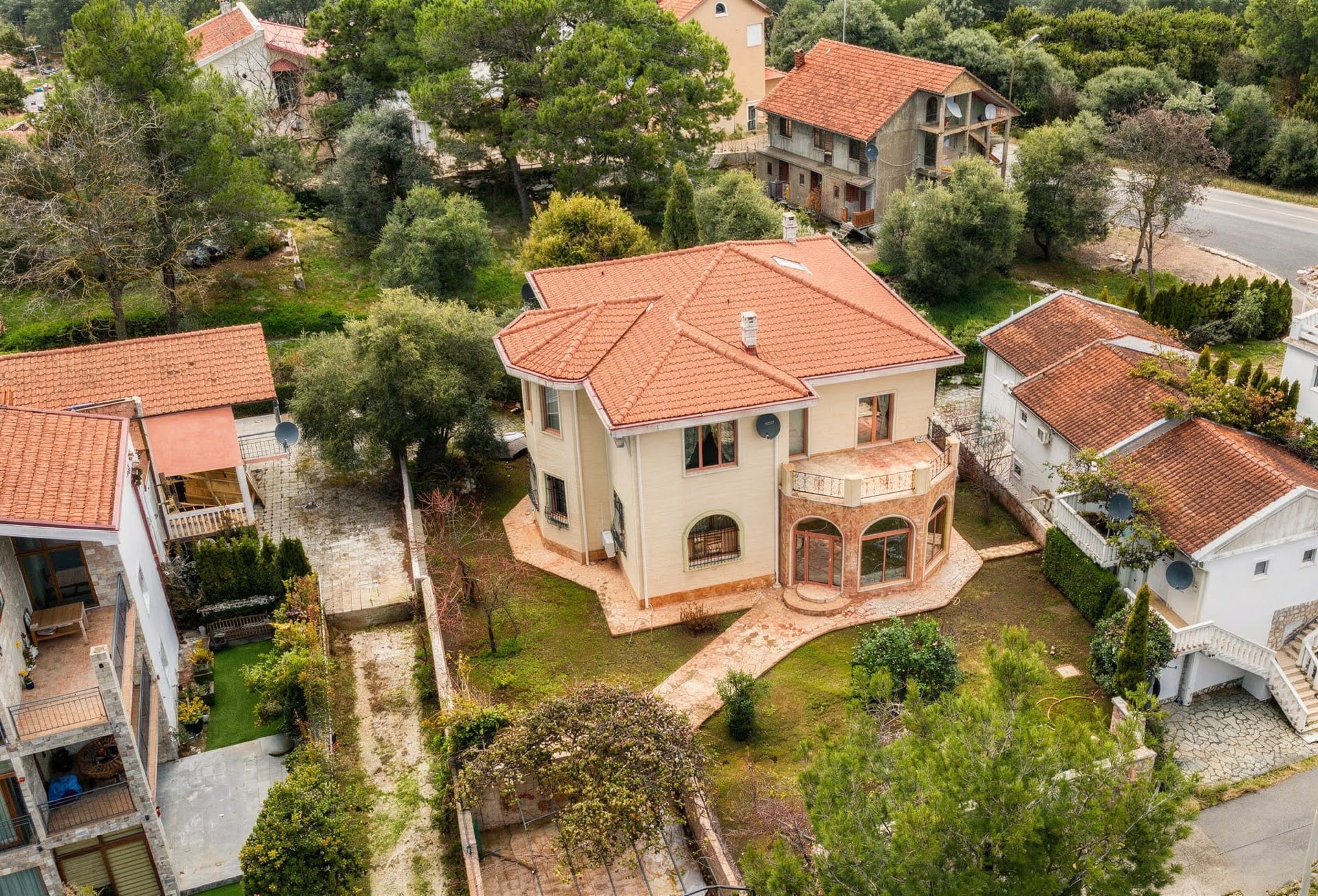 Pogled odozgo na dvospratnu vilu sa krovom od crepa i baštom u Luštici, Crna Gora: eksterijer kuće sa terasom.