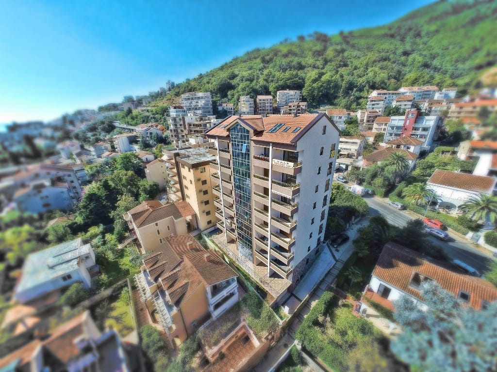 Pogled iz vazduha na višestambenu stambenu zgradu u Budvi, Crna Gora, sa panoramskim balkonima i krovom od crepa.