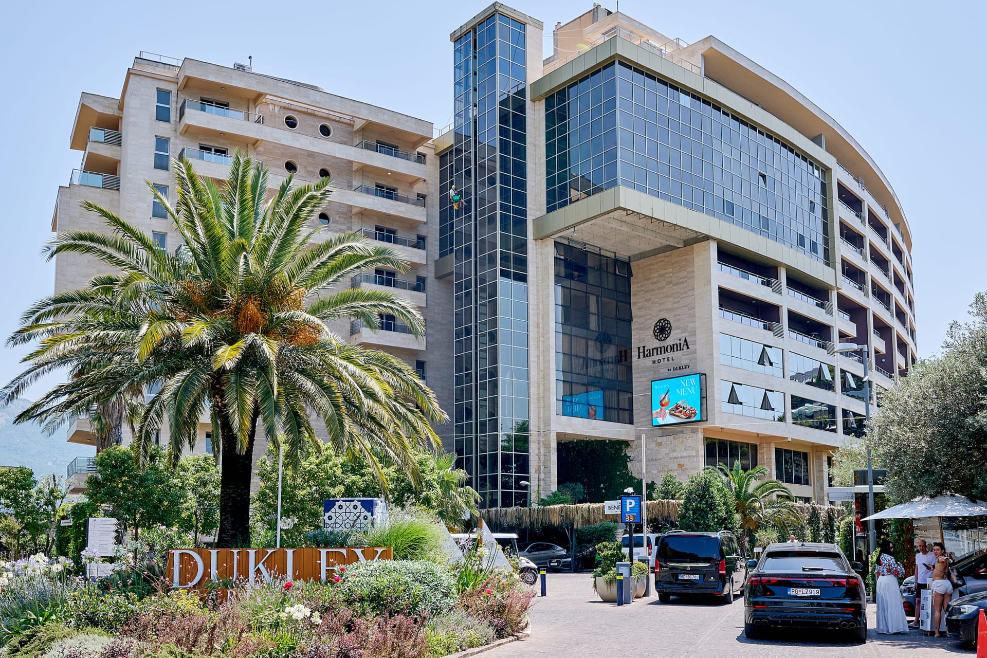Modernes Gebäude des Hotels Harmonia by Dukley in Bečići, Montenegro: Fassade mit Panoramaverglasung und Palmen am Eingang.