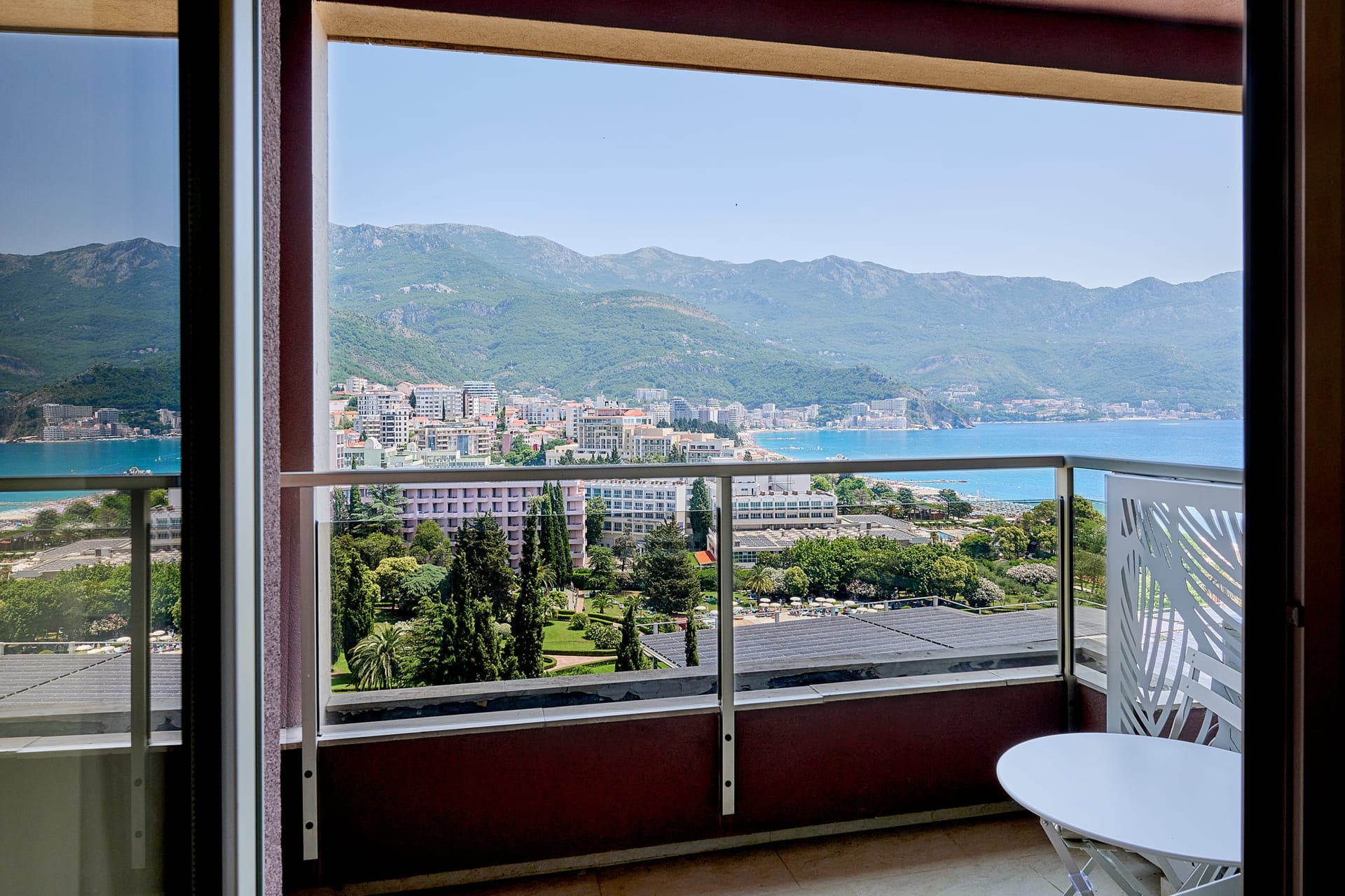 Blick vom Balkon der Apartments in Bečići, Montenegro: Panorama des Meeres, der Berge und der Ferienzone mit einem weißen Tisch.