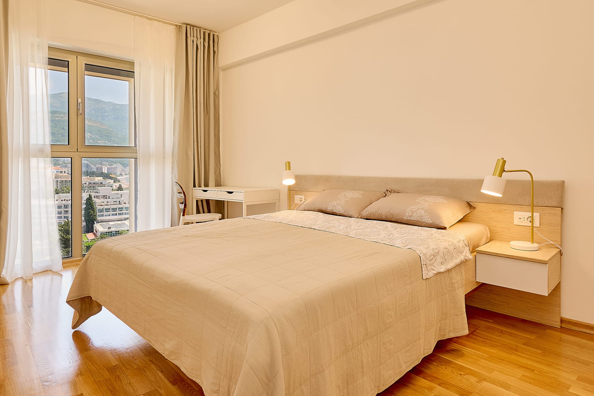 Gemütliches Schlafzimmer mit Doppelbett und Bergblick in einer Wohnung in Bečići, Montenegro. Helle Inneneinrichtung mit Parkettboden.