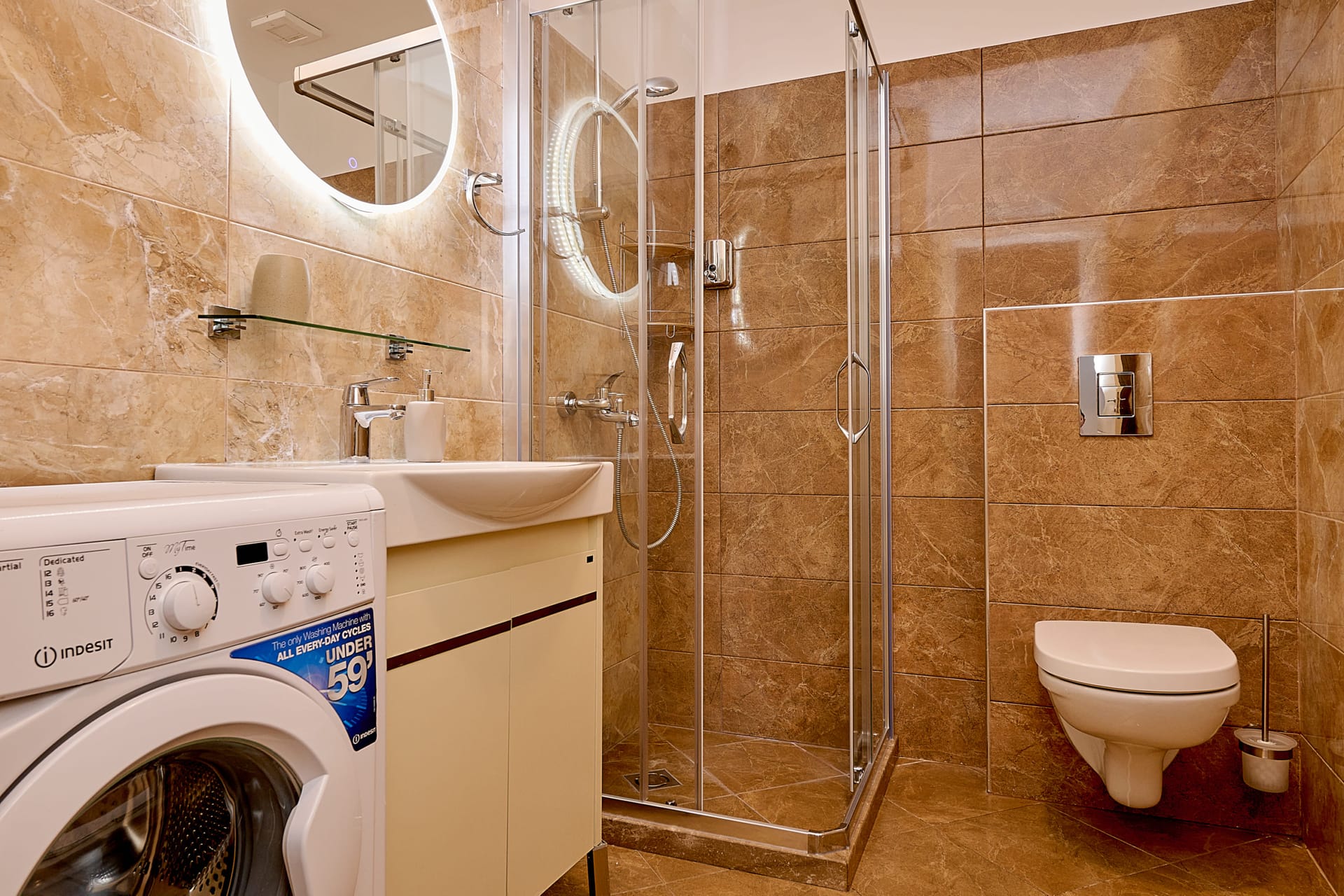 Modernes Badezimmer in einer Wohnung, Bečići, Montenegro: Duschkabine, Waschmaschine und beleuchteter Spiegel.