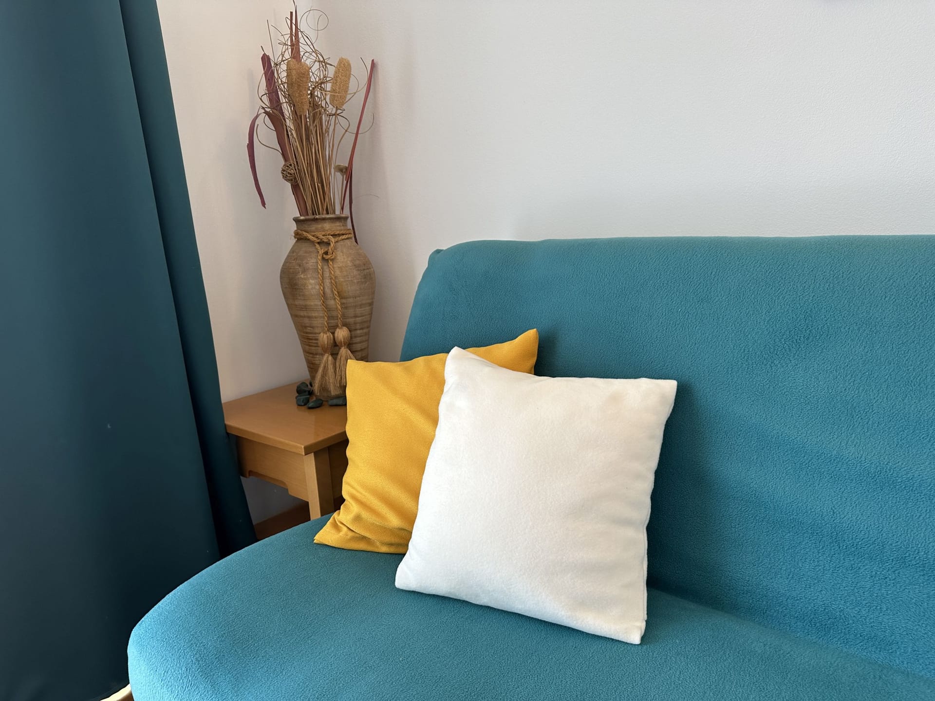 Tirkizni sofa sa dekorativnim jastucima u enterijeru apartmana u Bečićima, Crna Gora. Udobna dnevna soba sa dekorom.