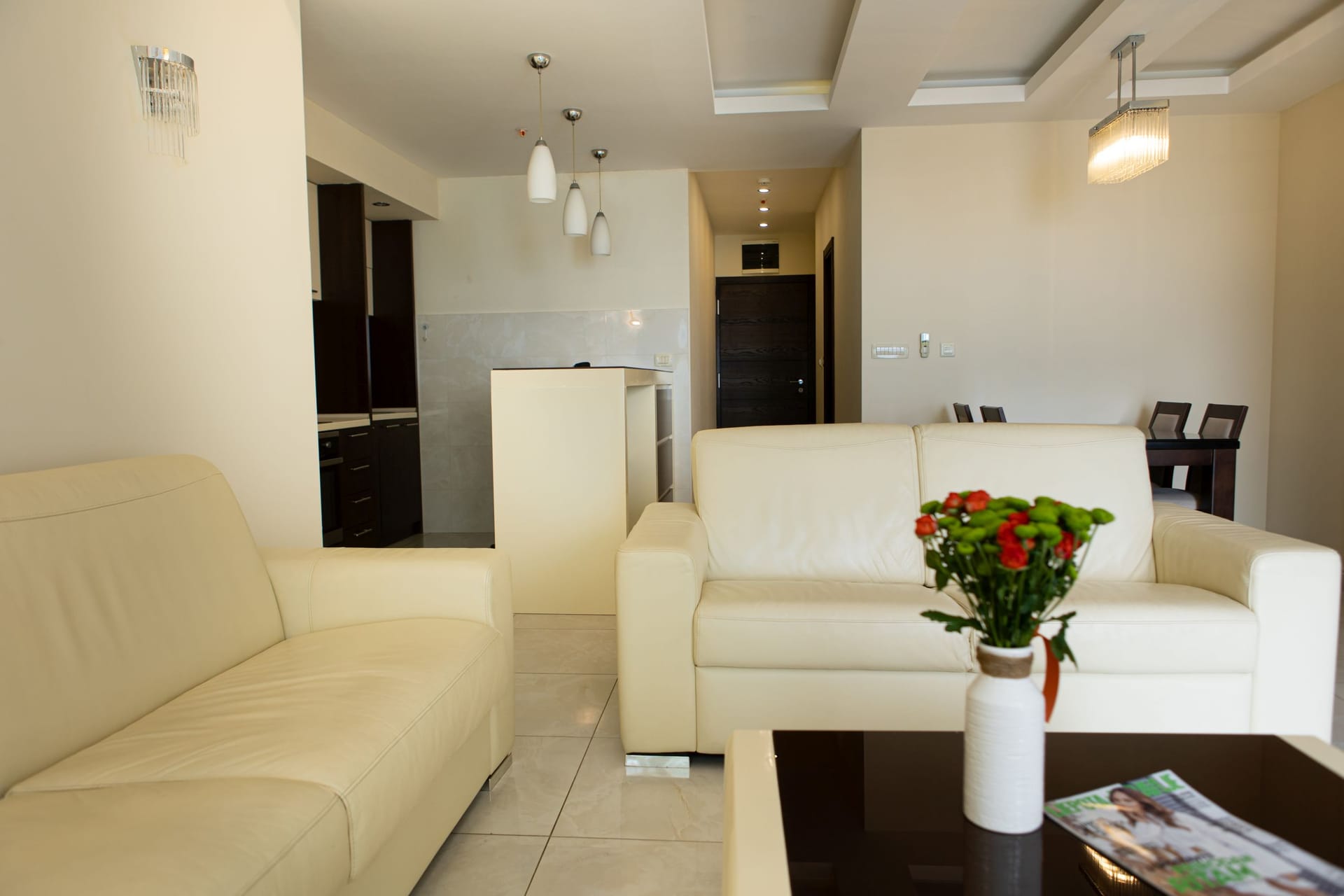 Jasny salon z skórzanymi kanapami i kuchnią w apartamencie w Bečići, Czarnogóra. Nowoczesne wnętrze z płytkami.