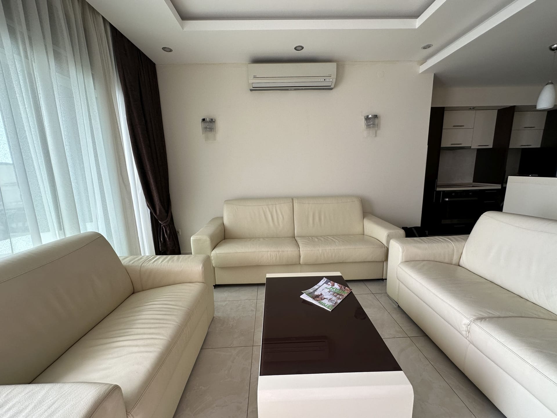 Salon z białymi skórzanymi kanapami i stolikiem kawowym w apartamencie w Bečići, Czarnogóra.