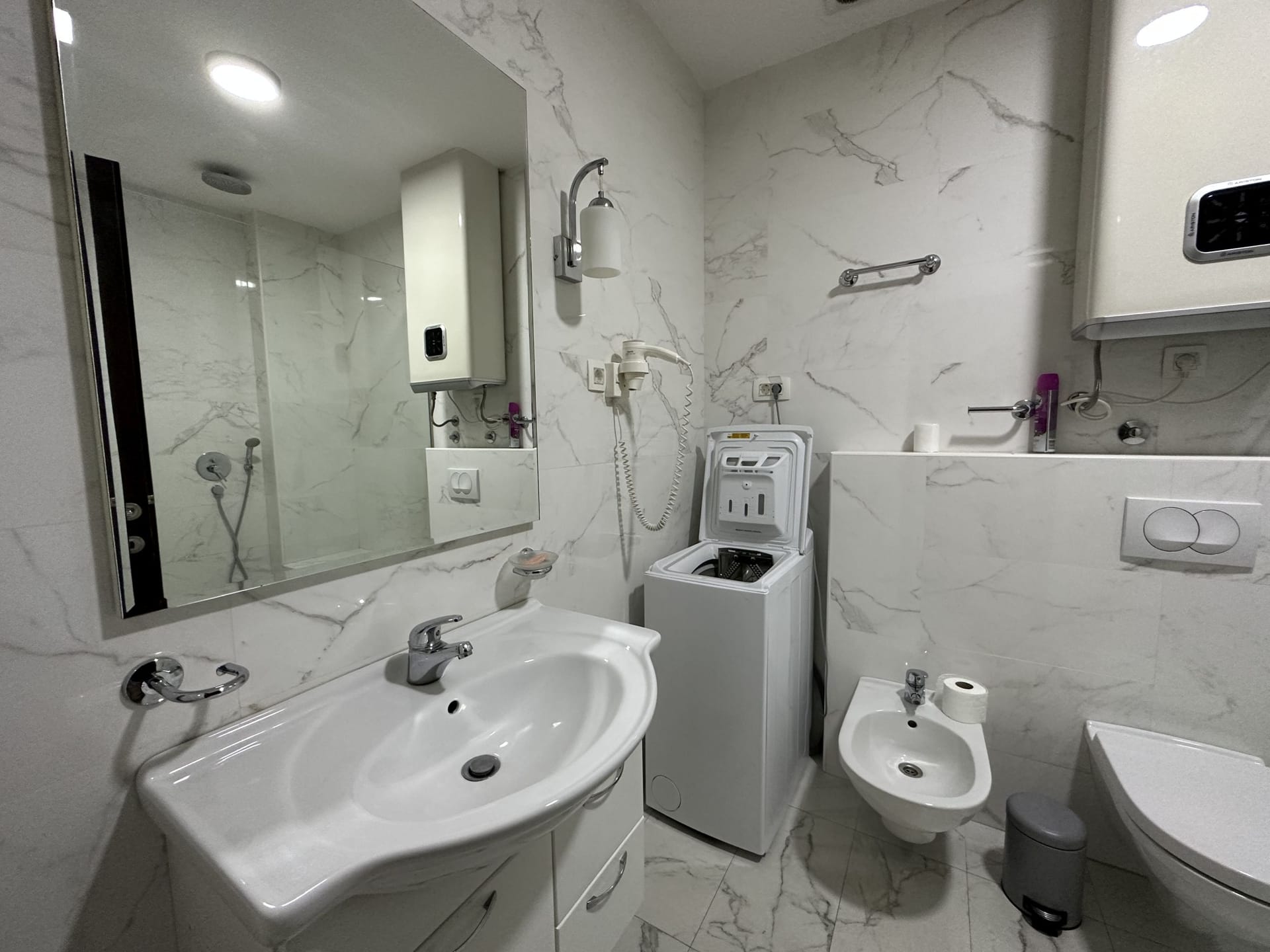 Nowoczesna łazienka w apartamencie w Bečici, Czarnogóra: jasne płytki imitujące marmur, armatura sanitarna i pralka.