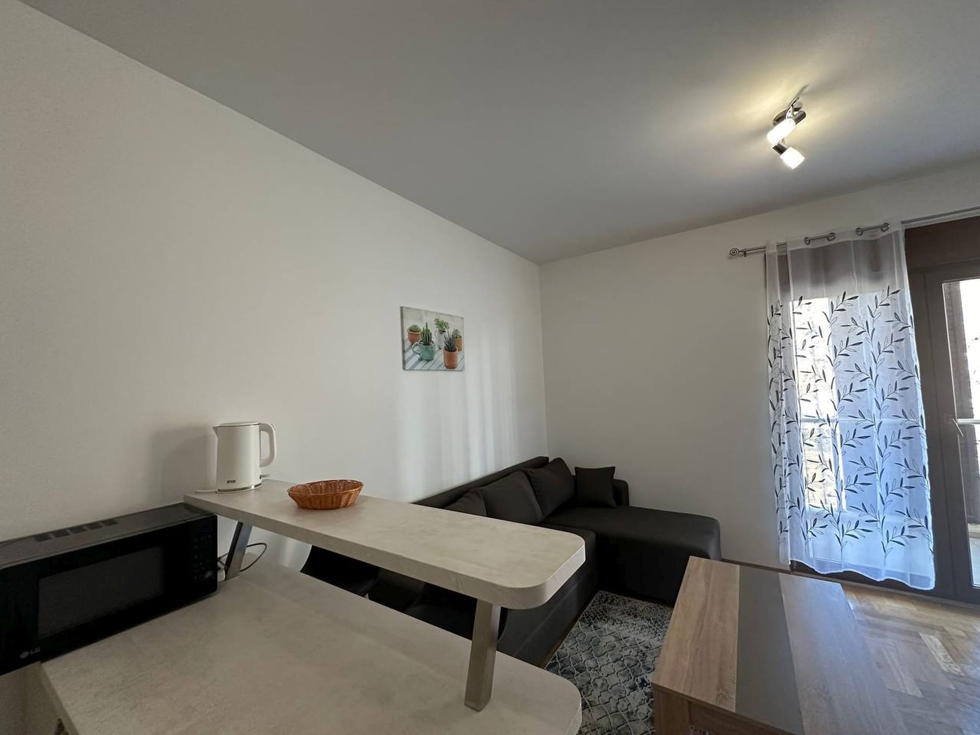 Dnevna soba u apartmanima Bečići, Crna Gora: moderan nameštaj, barski pult, ugaona sofa i izlaz na balkon.