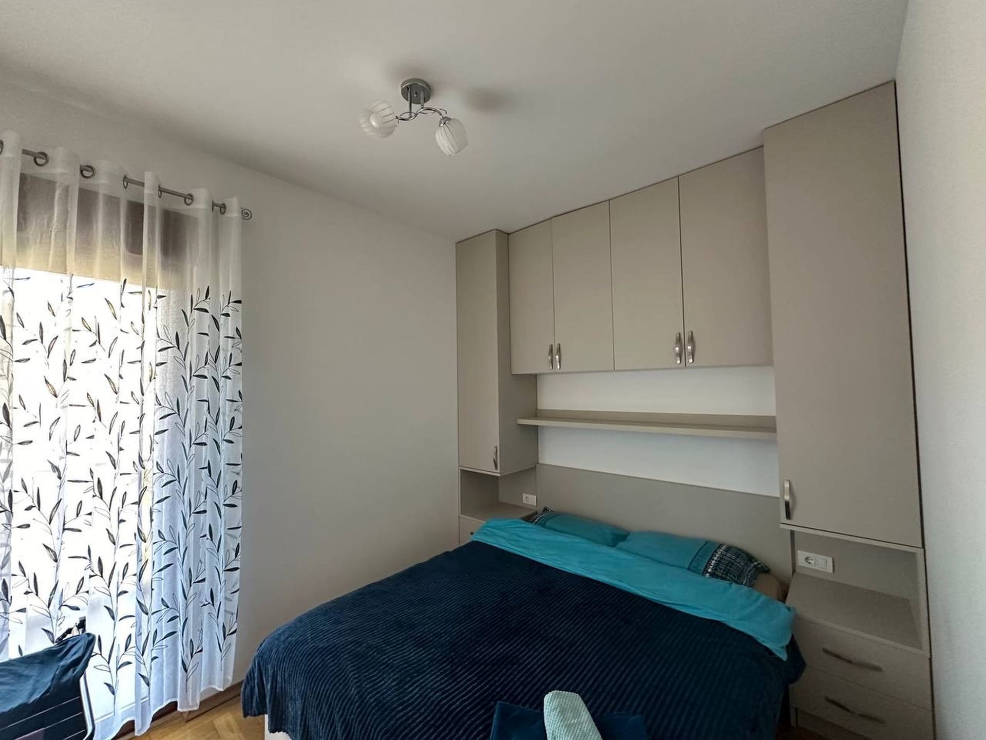 Spavaća soba u apartmanima u Bečićima, Crna Gora: bračni krevet, ugradbeni ormar bež boje i prozor sa tilom.