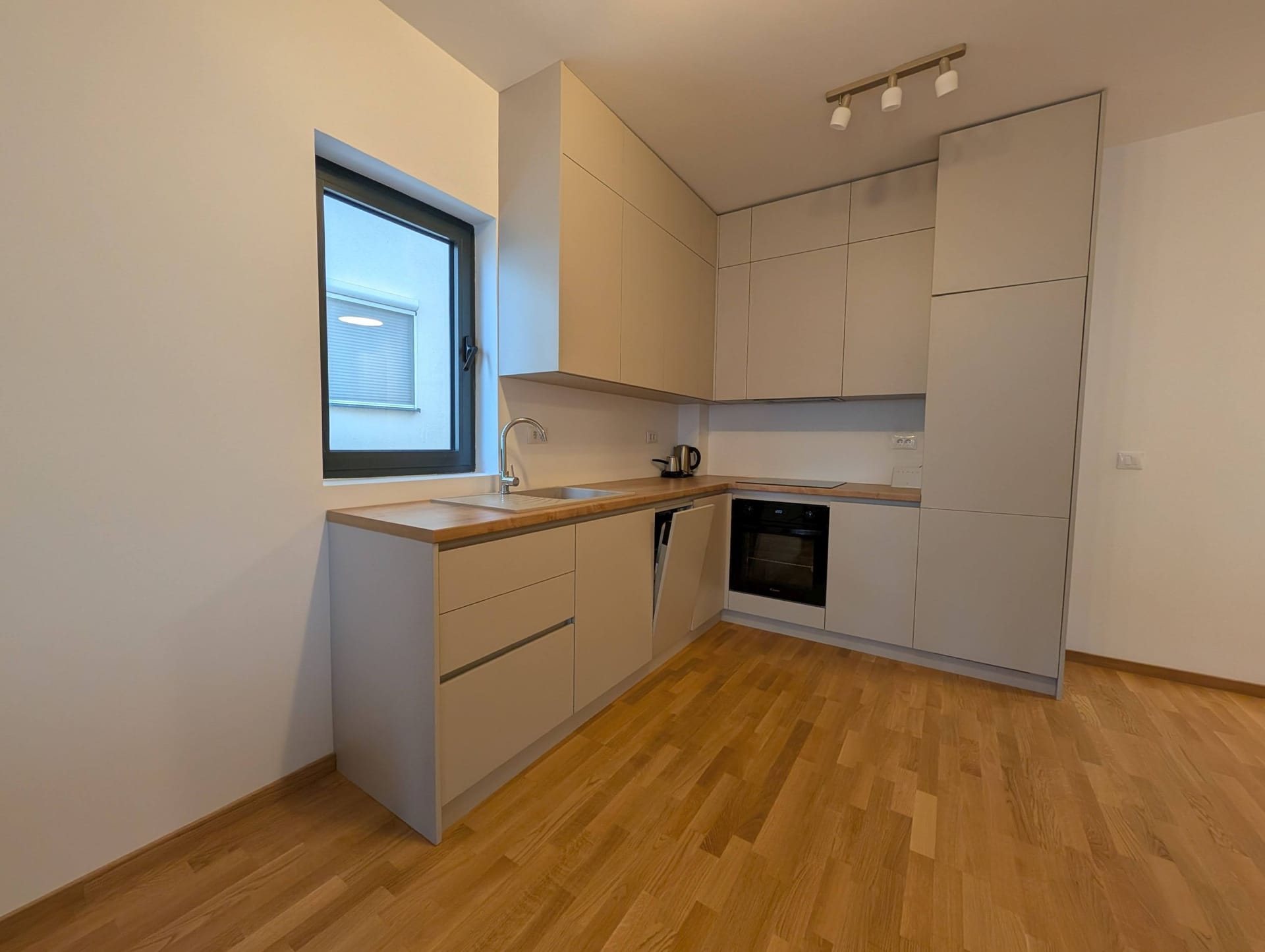 Moderna svetla kuhinja sa drvenom radnom pločom u apartmanima u Bečićima, Crna Gora. Ugrađeni uređaji i parket.