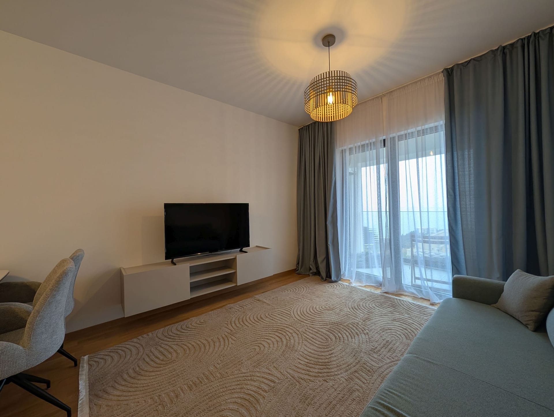 Moderna dnevna soba u apartmanima Bečići, Crna Gora: sofa, TV zona, tepih i izlaz na terasu sa pogledom na more.