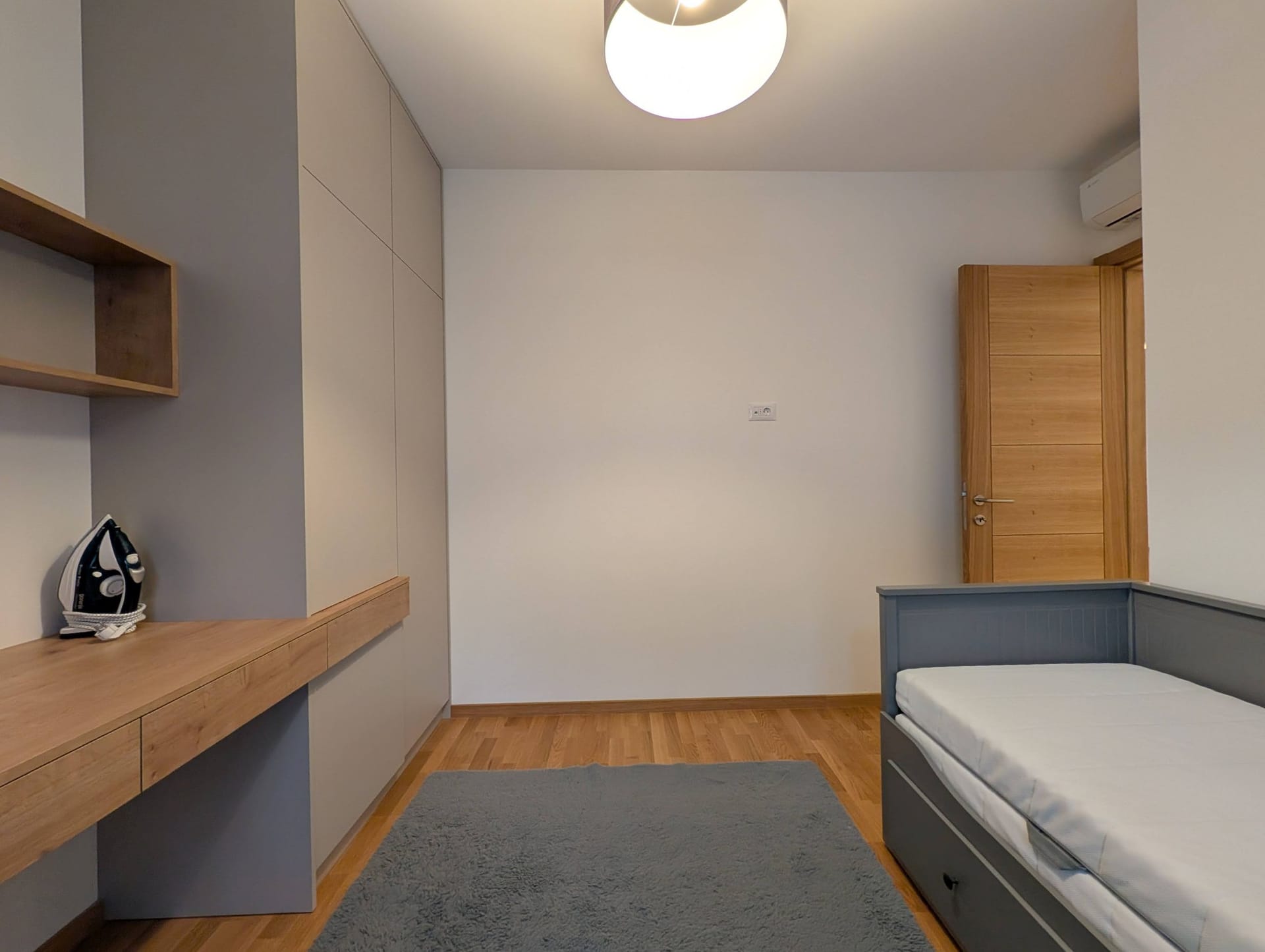 Moderna spavaća soba u stanu u Bečićima, Crna Gora: ugradbeni ormar, radni sto, krevet i parket.
