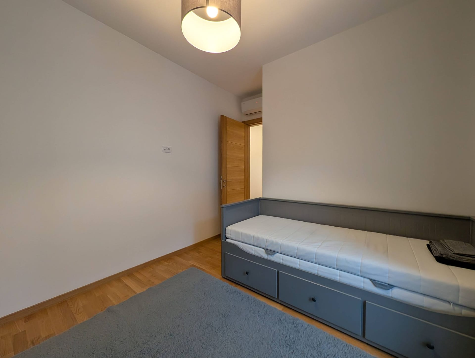 Svetla spavaća soba sa sivim krevetom i parketom u apartmanima u Bečićima, Crna Gora. Moderan enterijer sa klima uređajem.