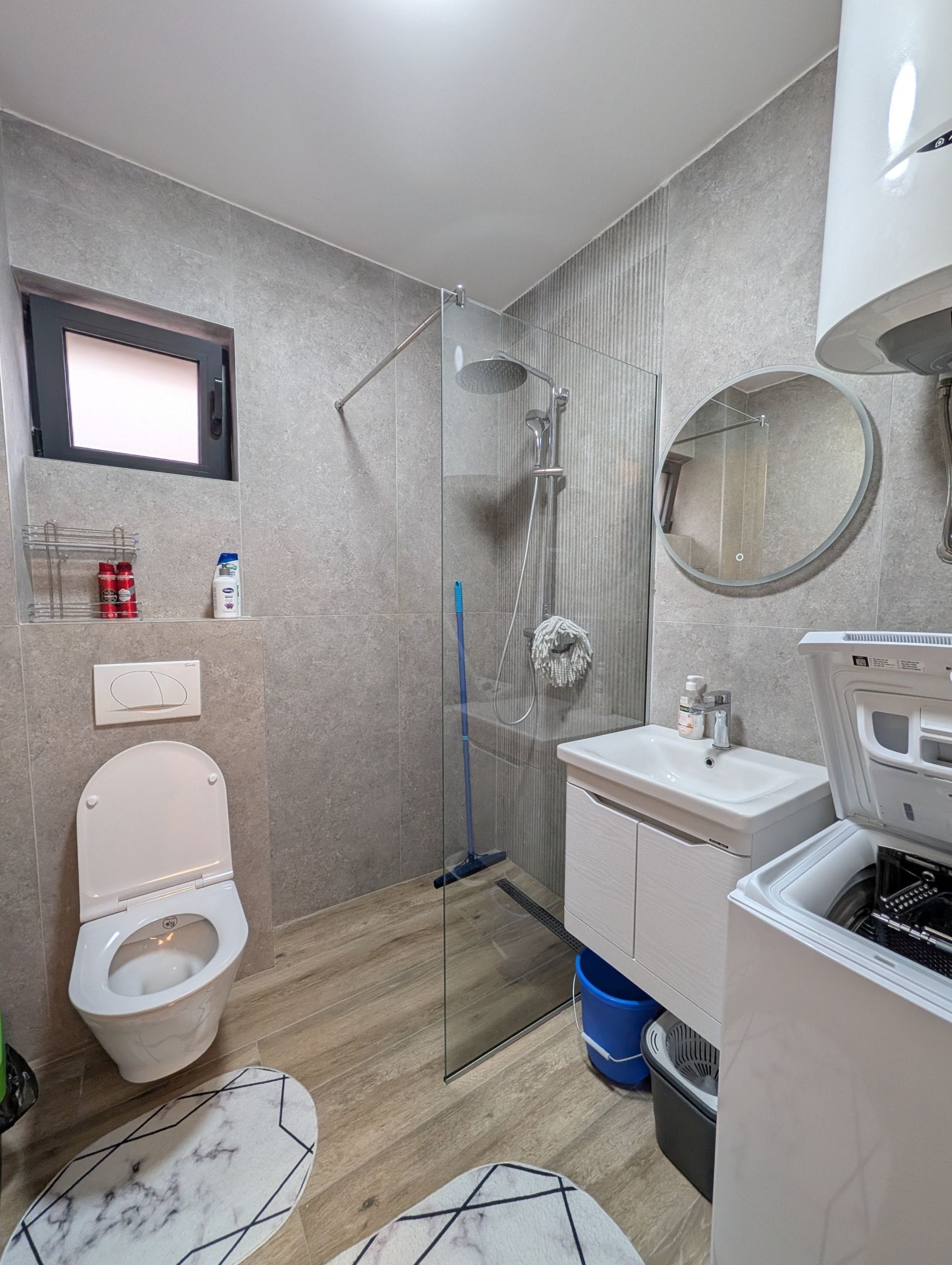 Moderno kupatilo u apartmanima, Bečići, Crna Gora: tuš kabina, veš mašina i sive pločice.