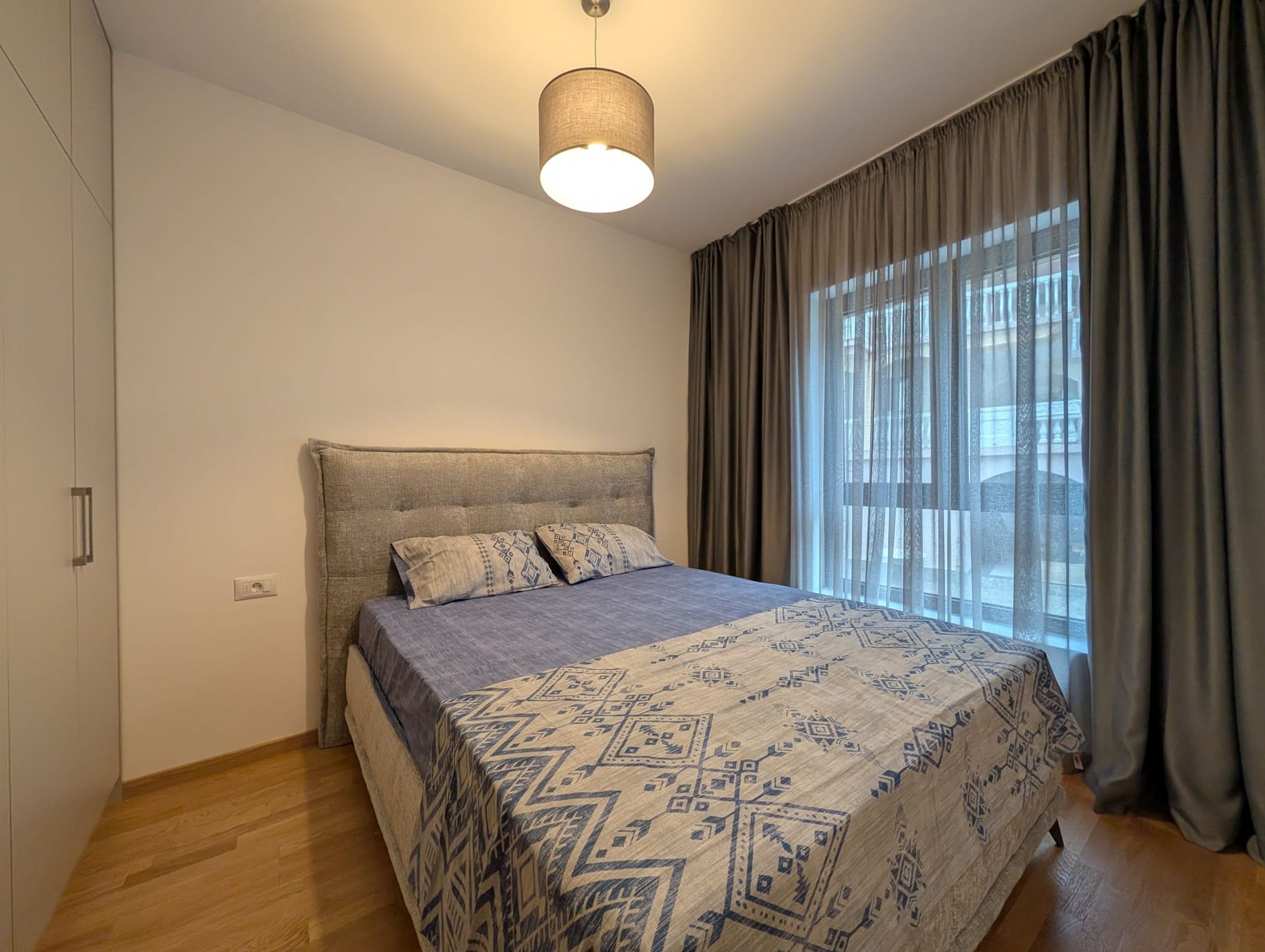 Moderna spavaća soba sa bračnim krevetom u apartmanima u Bečićima, Crna Gora: svetli enterijer, parket i zavese.