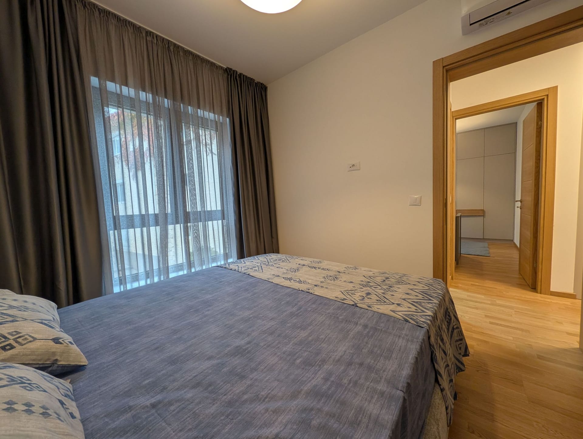 Moderna spavaća soba sa bračnim krevetom u apartmanima Bečići, Crna Gora: svetla završna obrada i parket.
