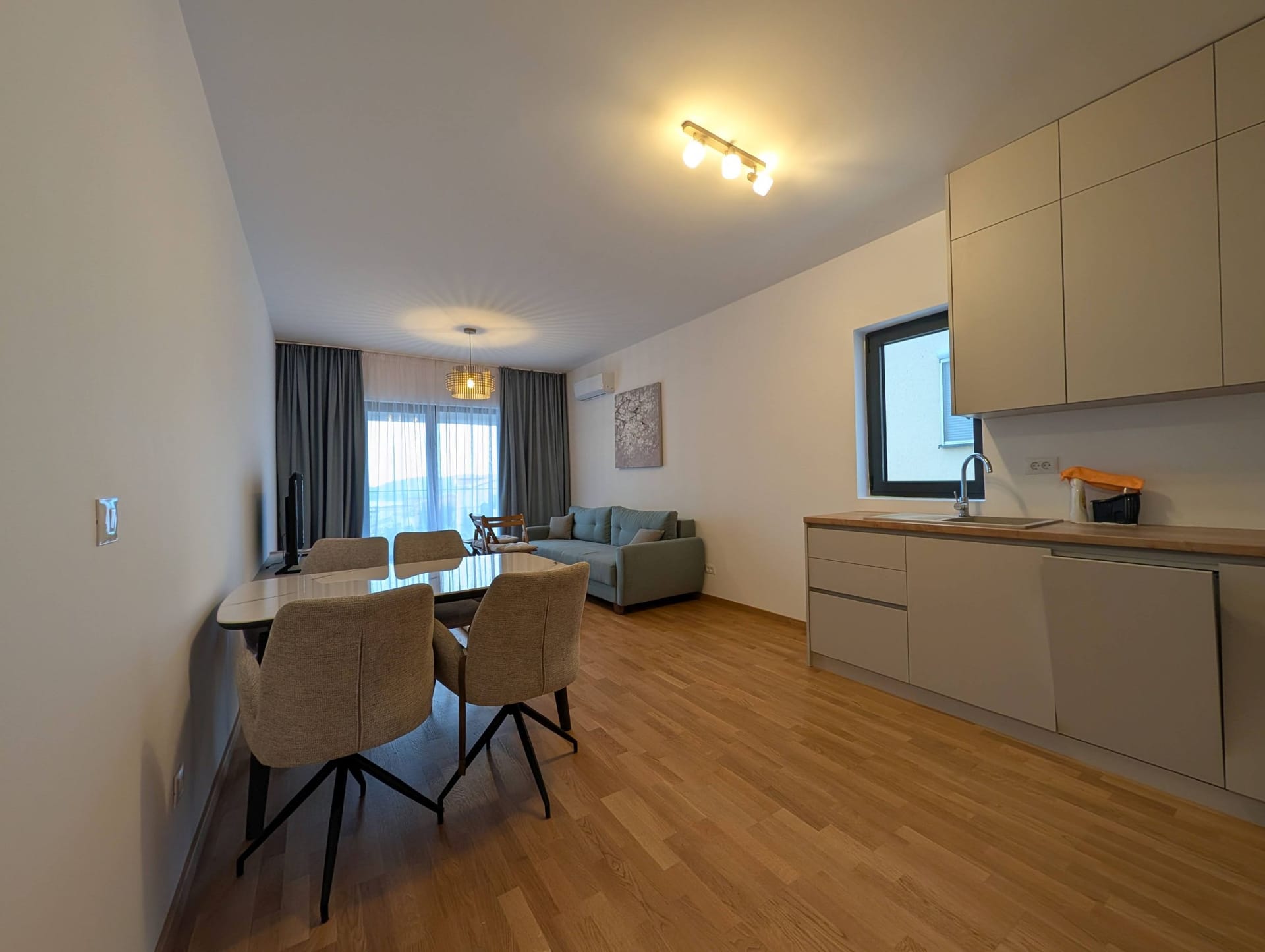 Moderna dnevna soba sa kuhinjom u apartmanima Bečići, Crna Gora: trpezarijski prostor, sofa i stilsko uređenje enterijera.