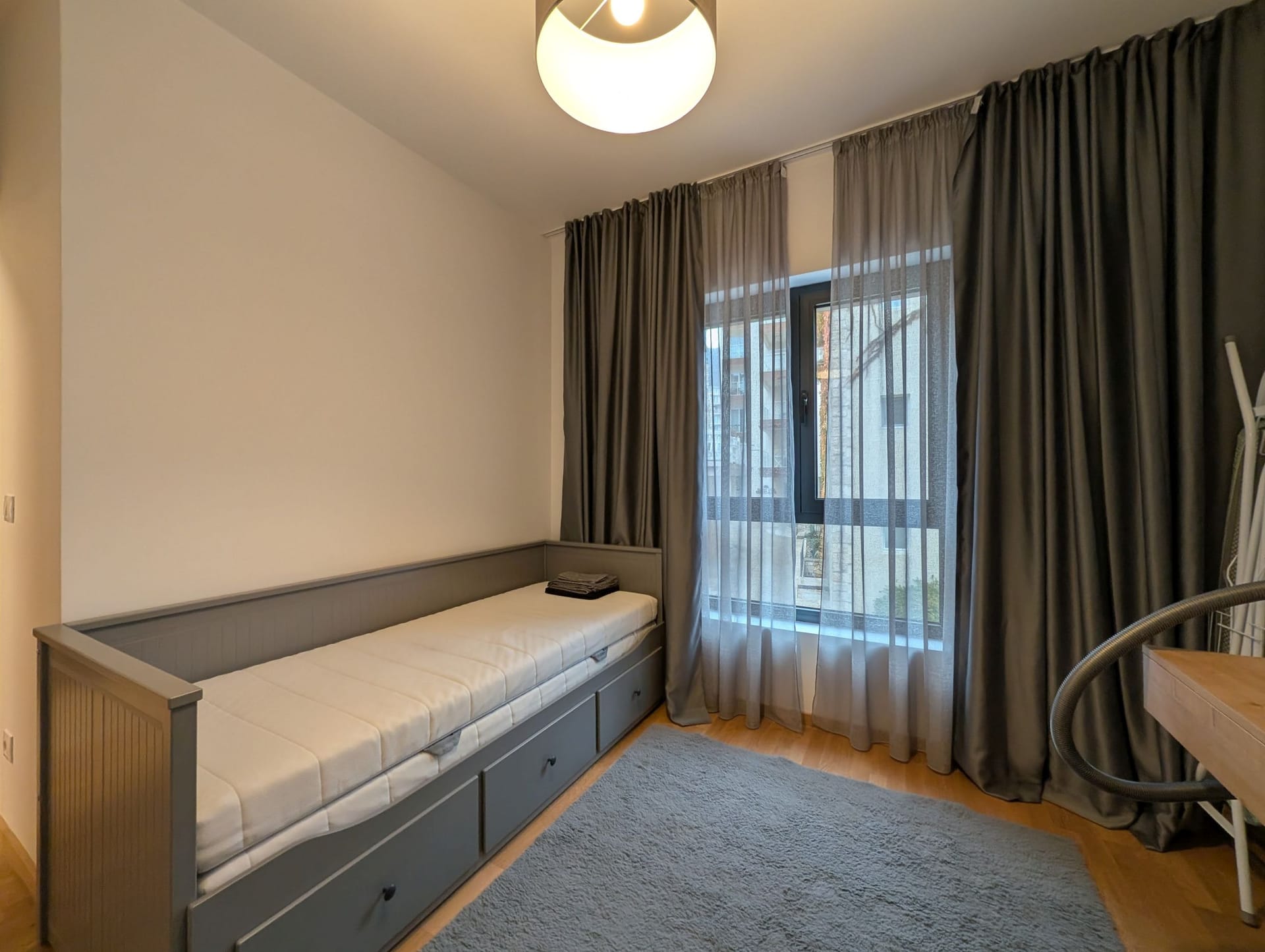 Spavaća soba sa sivim krevetom i debelim zavesama u apartmanima u Bečićima, Crna Gora. Moderan enterijer sa tepihom.