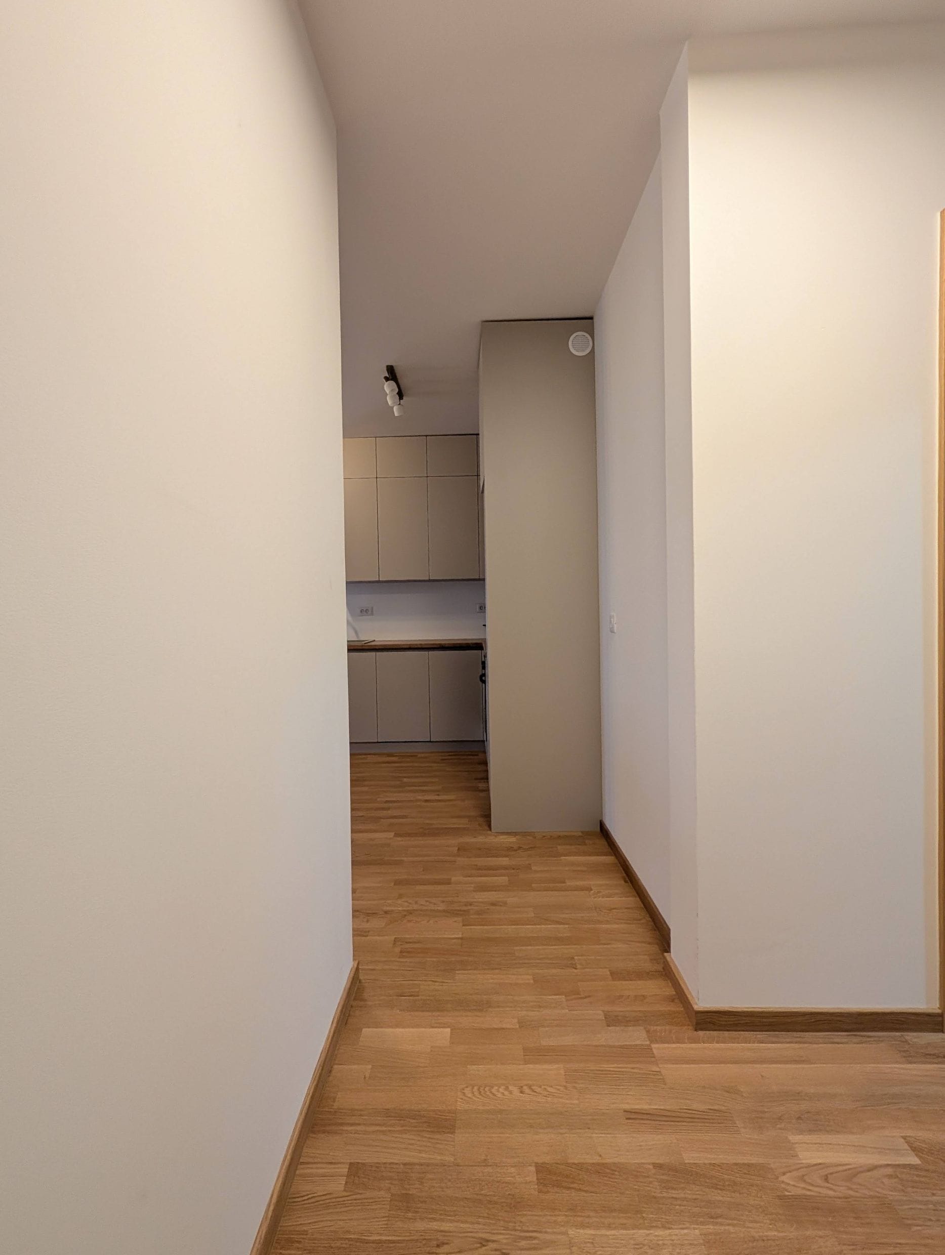 Moderna kuhinja u svetlim tonovima sa drvenim podom u apartmanima, Bečići, Crna Gora. Pogled iz hodnika na kuhinjski element.