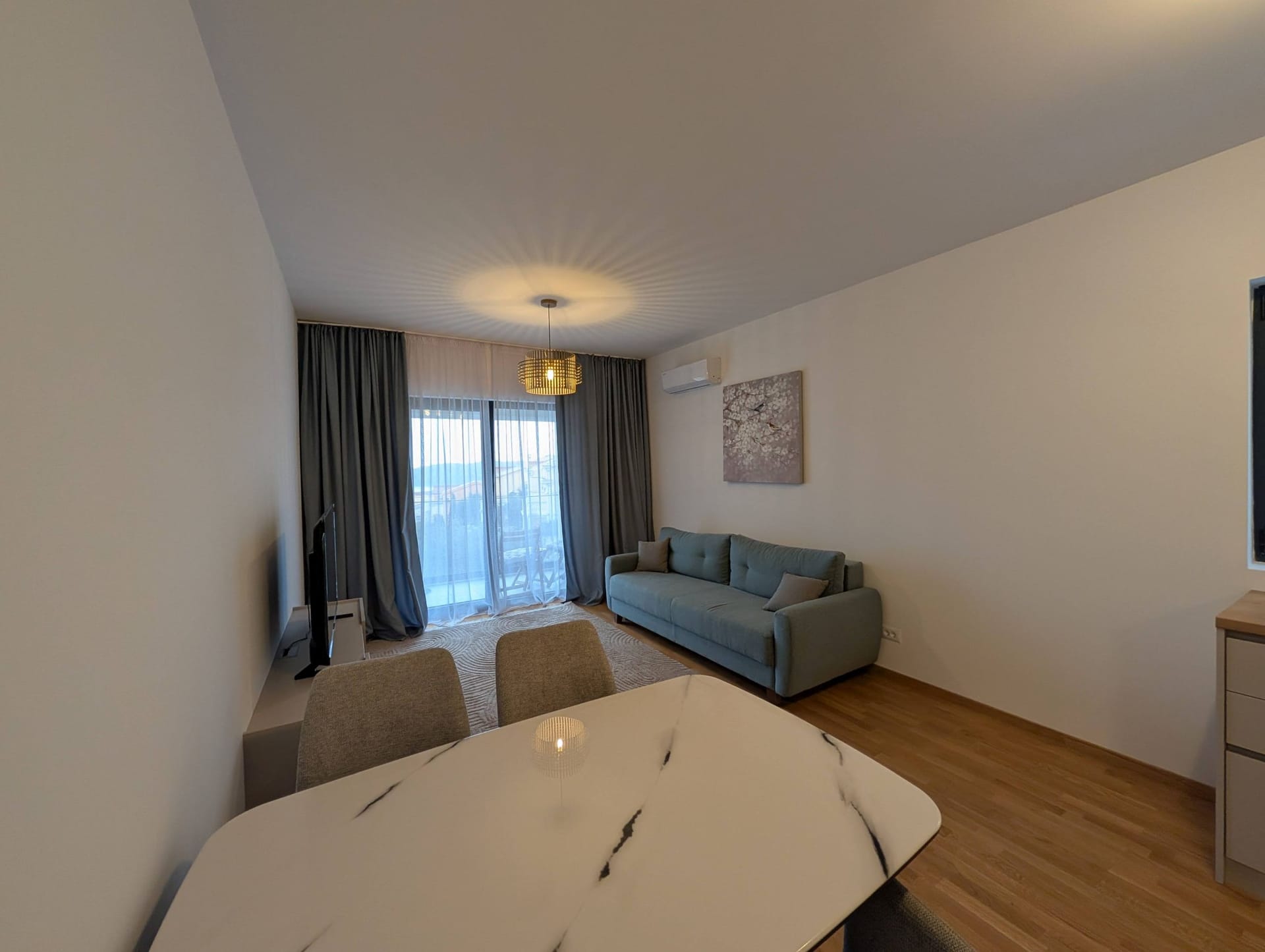Moderna dnevna soba u apartmanima Bečići, Crna Gora: trpezarijski sto, sivi sofa, panoramski prozor i stilski dekor.