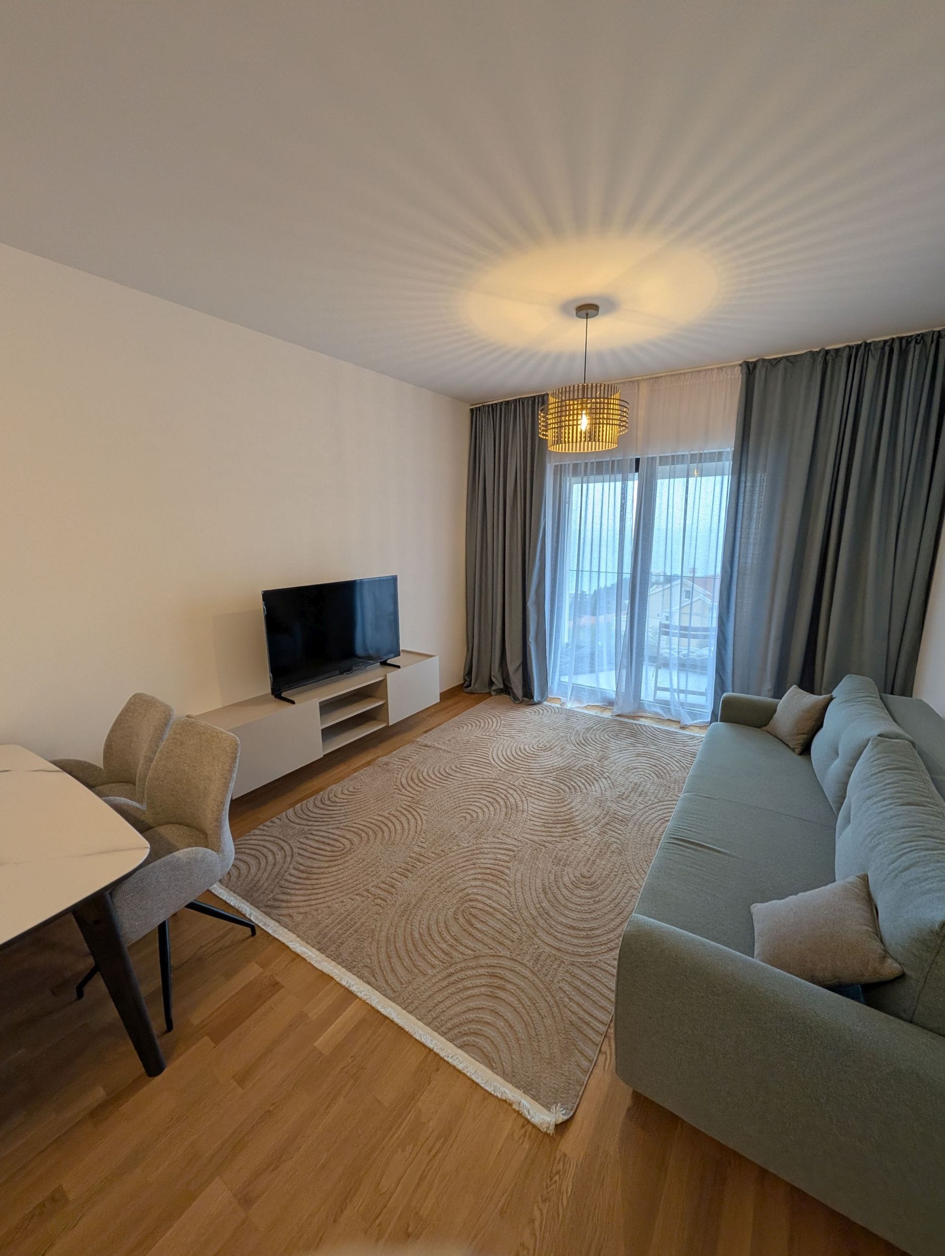 Moderna dnevna soba u apartmanima Bečići, Crna Gora: sofa, TV zona, trpezarijski sto i izlaz na balkon sa pogledom.