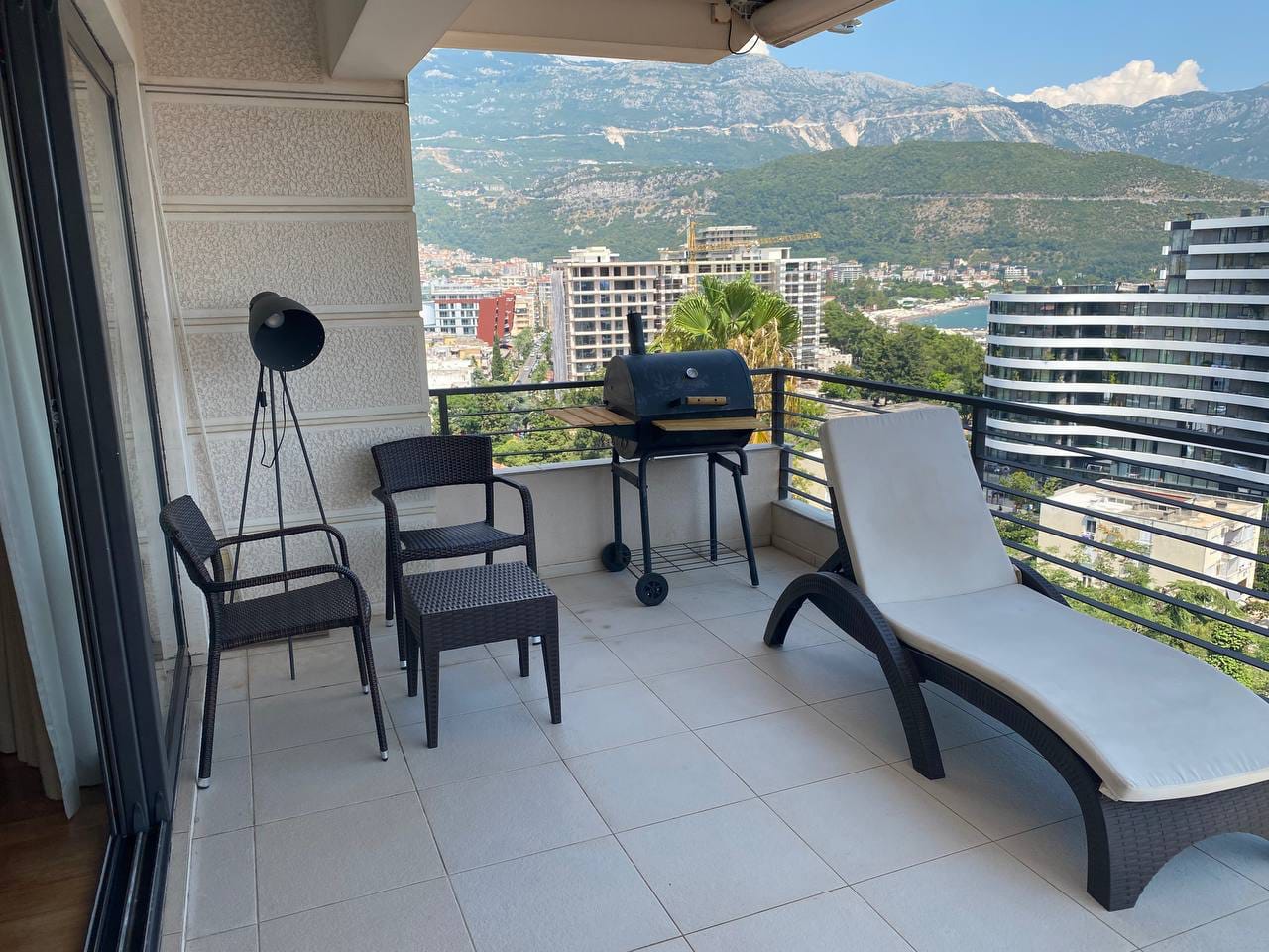 Terasa stana u Budvi, Crna Gora: pletene fotelje, ležaljka, roštilj i panoramski pogled na planine i more.