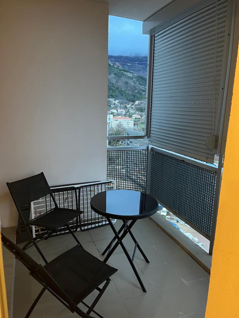Balkon sa nameštajem i pogledom na planine u stanu, Budva, Crna Gora. Udobna terasa sa crnim stolom i stolicama.