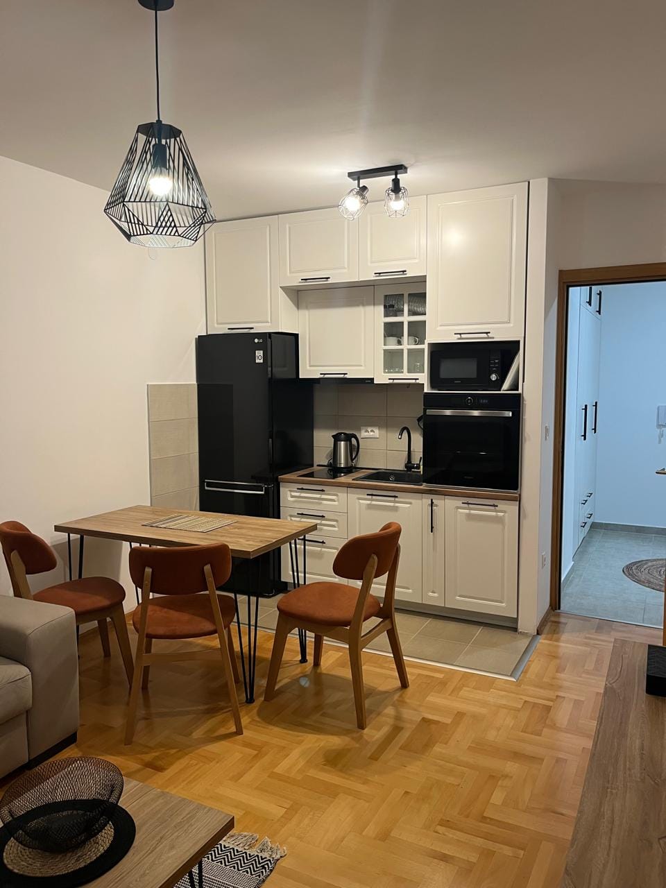 Moderna kuhinja u stanu u Budvi, Crna Gora: beli frontovi, crna tehnika, trpezarijska zona i parket.