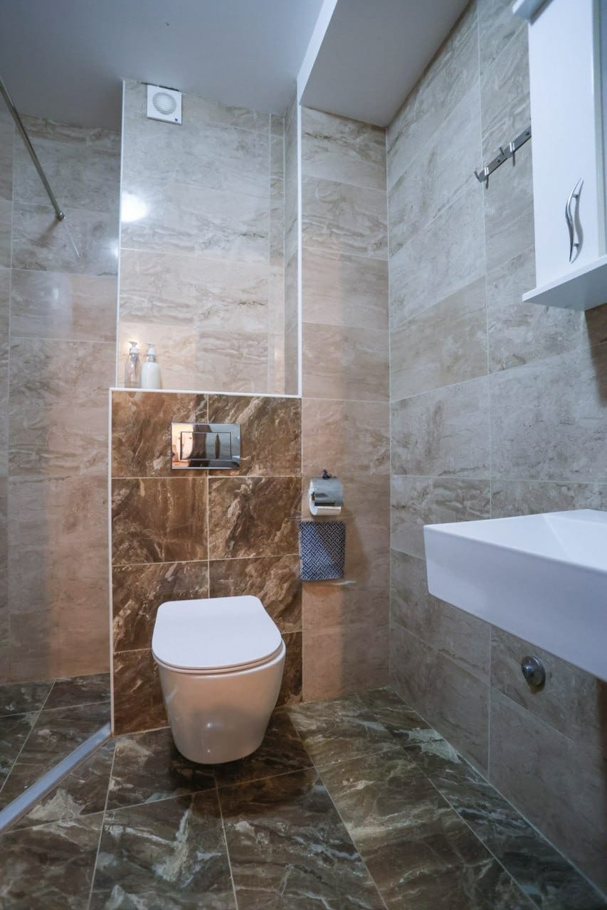 Savremeno kupatilo u stanu u Budvi, Crna Gora: bež pločice, viseća WC šolja i tuš zona.