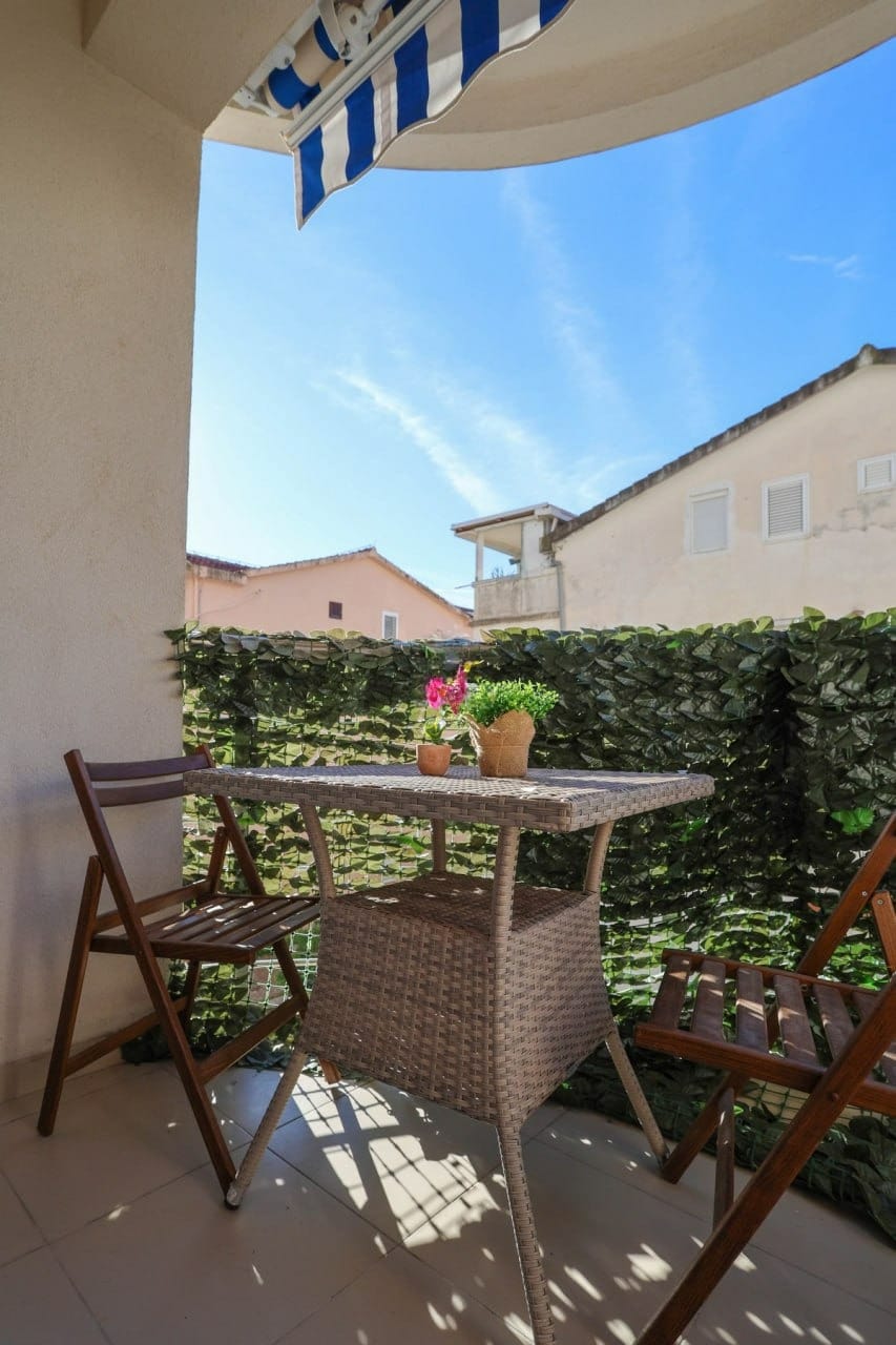 Ugodan balkon s pletenim nameštajem i markizom u stanu u Budvi, Crna Gora, s pogledom na grad i sunčanom terasom.