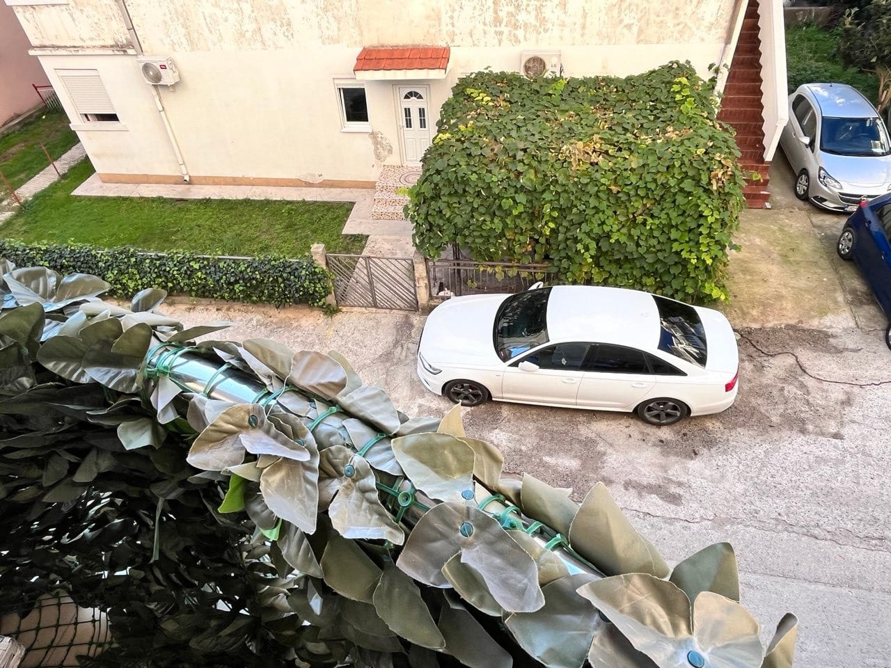 Pogled sa balkona na privatnu kuću sa parkingom i zelenom baštom u Budvi, Crna Gora. Stan sa sopstvenim parkingom.