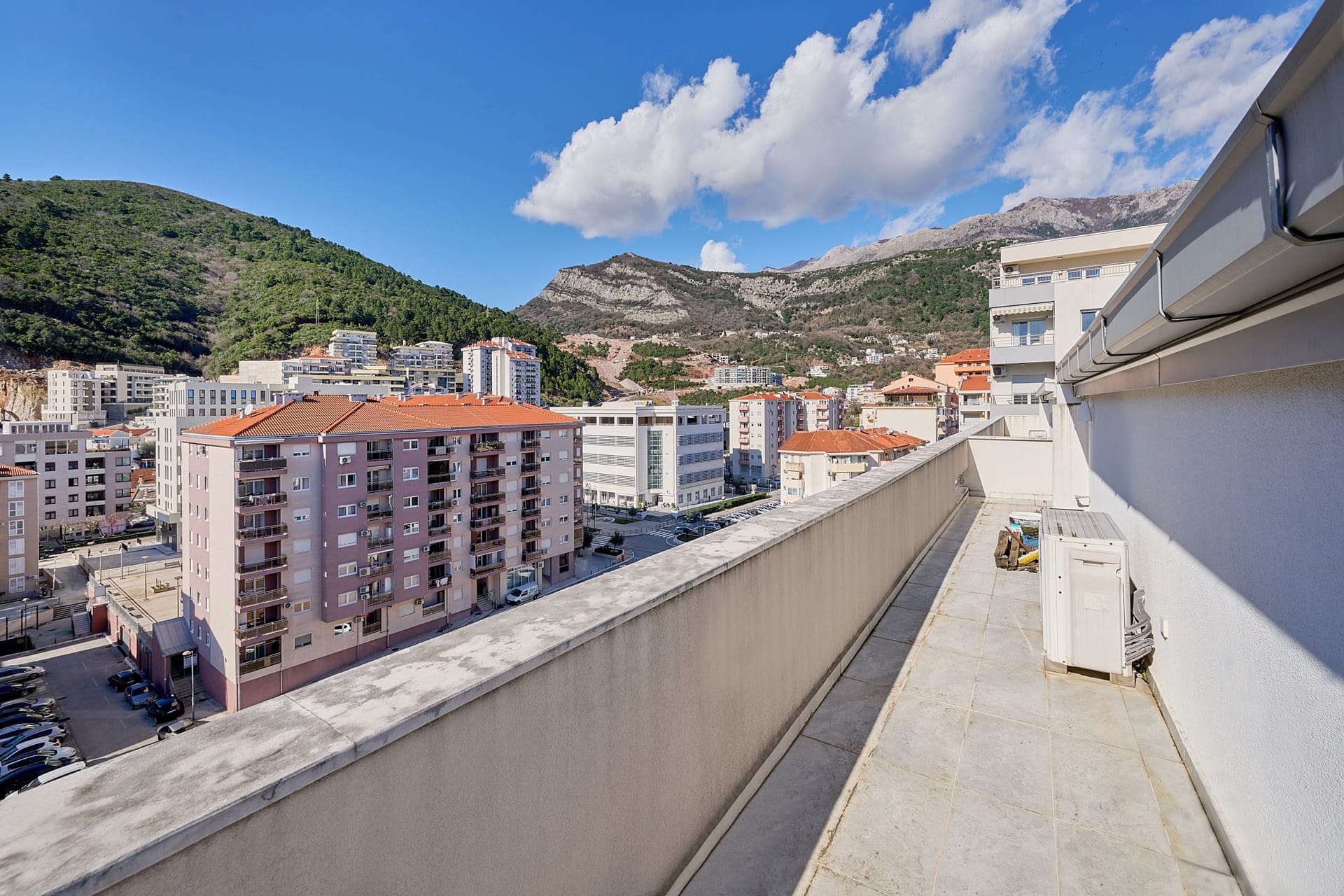 Prostran balkon stana u Budvi, Crna Gora, sa panoramskim pogledom na gradske kuće i planinski pejzaž.